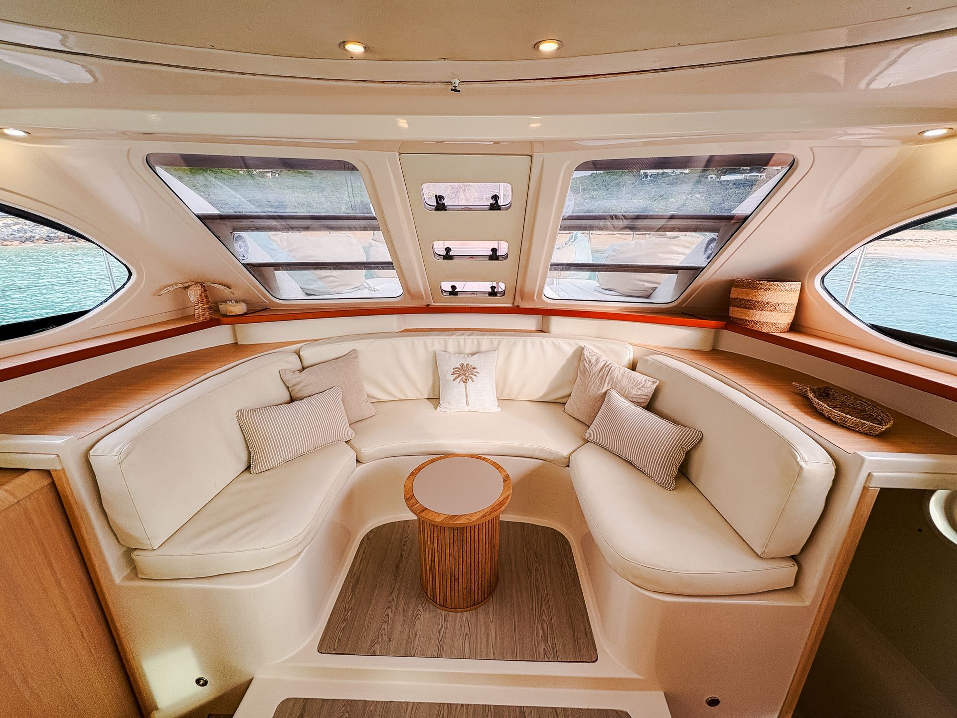 Interior view of a boat lounge with cream-colored seating, windows, and a wood side table.
