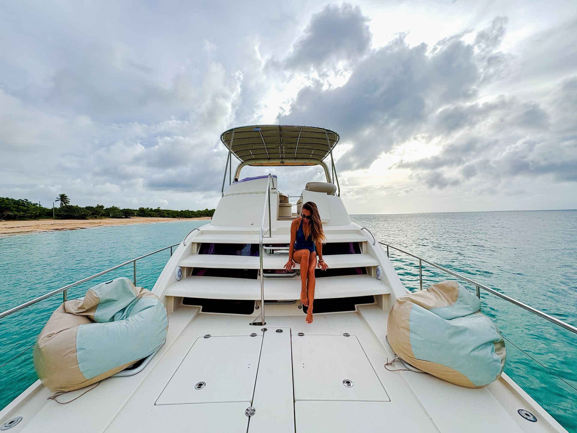 Woman sitting on boat steps, turquoise water, cloudy sky, beanbag chairs.