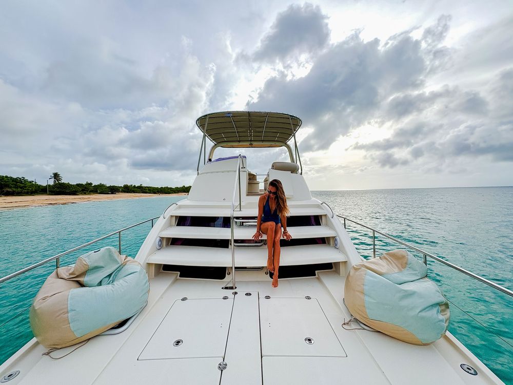 Woman sitting on boat steps, turquoise water, cloudy sky, beanbag chairs.
