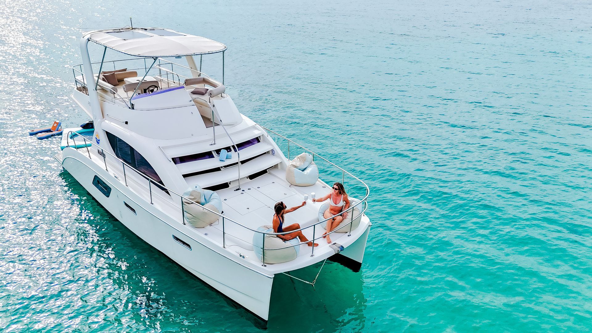 Catamaran on turquoise water, two people relaxing on deck. Sunny day.
