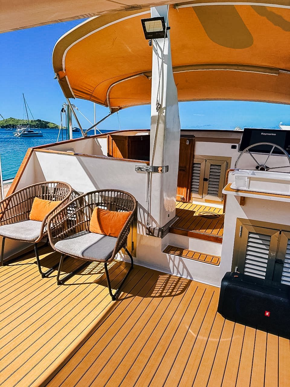 Boat deck with wicker chairs, cushions, and sunshade overlooking the sea.