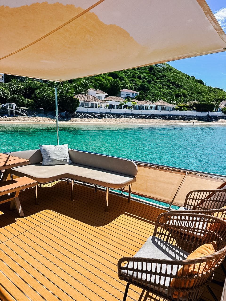 A boat deck with seating, canopy, and view of turquoise water and shoreline under a sunny sky.