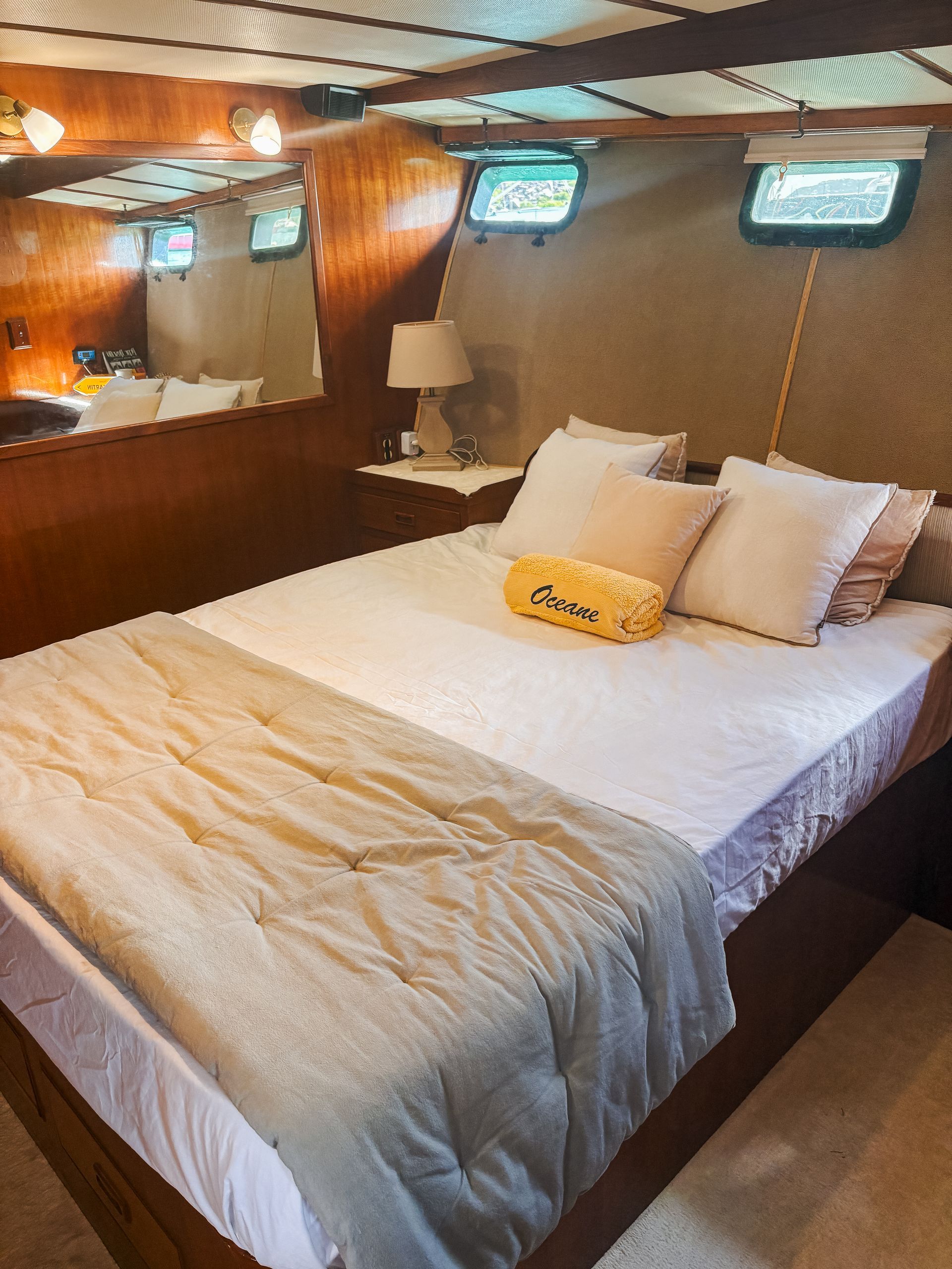 A bedroom inside a boat. It has a bed, windows, and wood paneling.