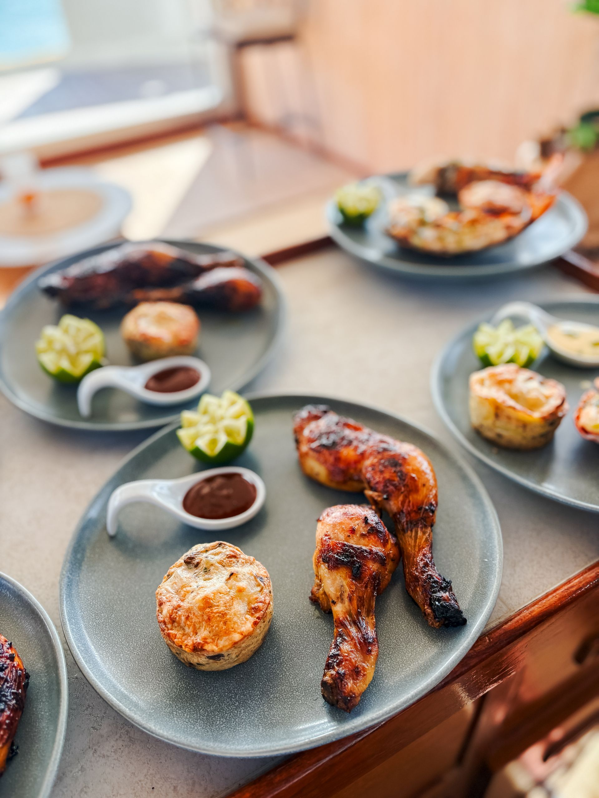 Plates of grilled chicken, lime wedges, and small pastries with dipping sauce on a table.
