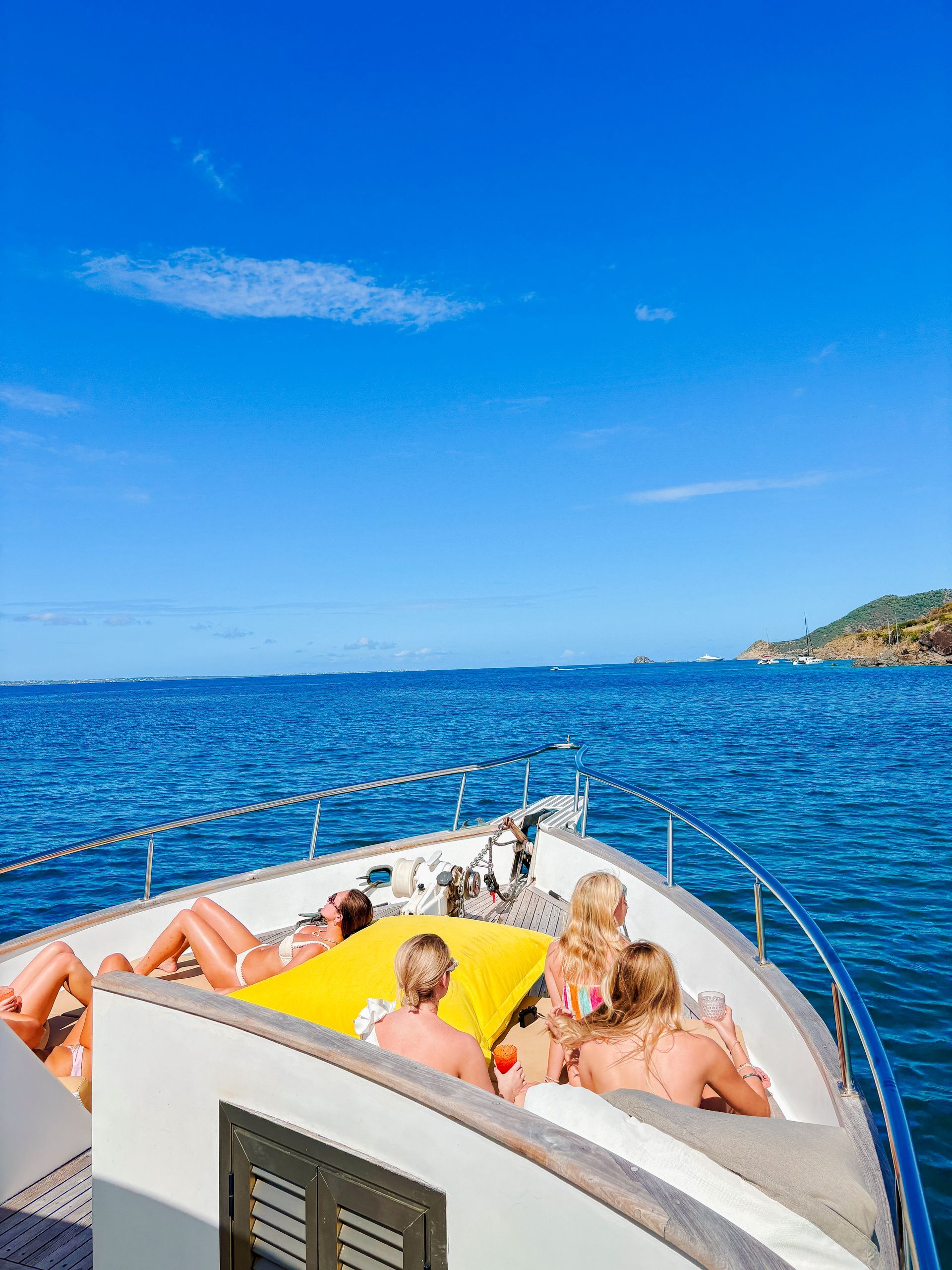 People sunbathe on the deck of a boat under a bright blue sky on the ocean.