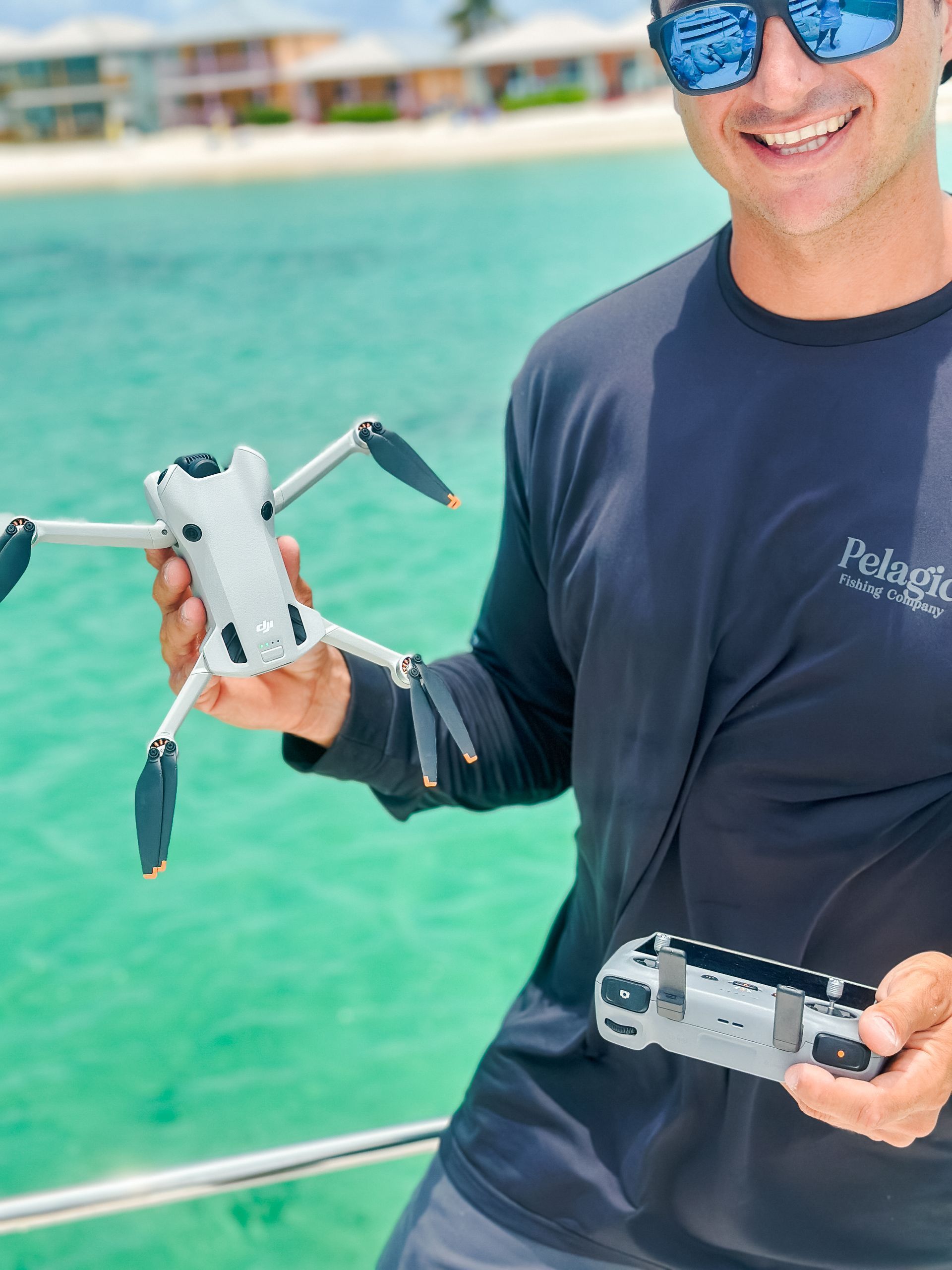 Man on boat holding a drone and remote, turquoise water in background. Sunny day.