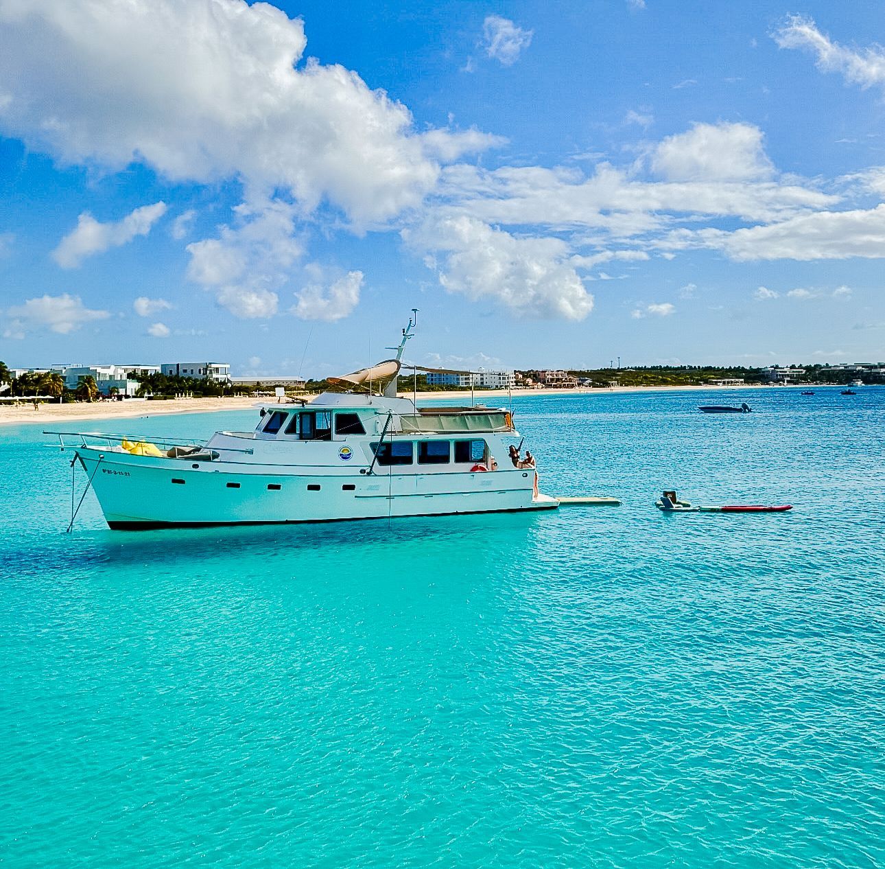 White boat anchored in turquoise water near a beach under a blue sky with clouds.