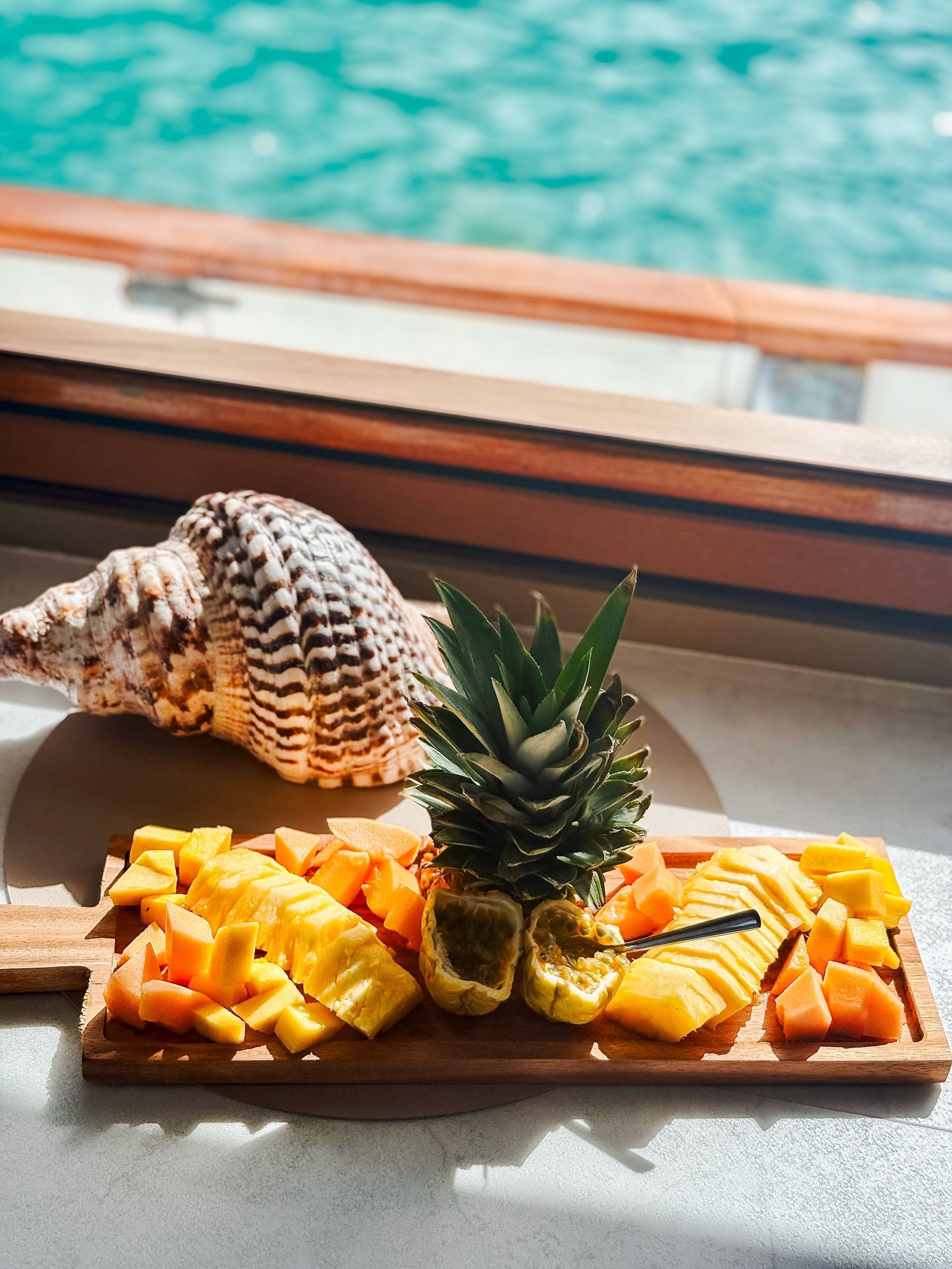 Wooden platter of tropical fruit with a seashell, ocean background.
