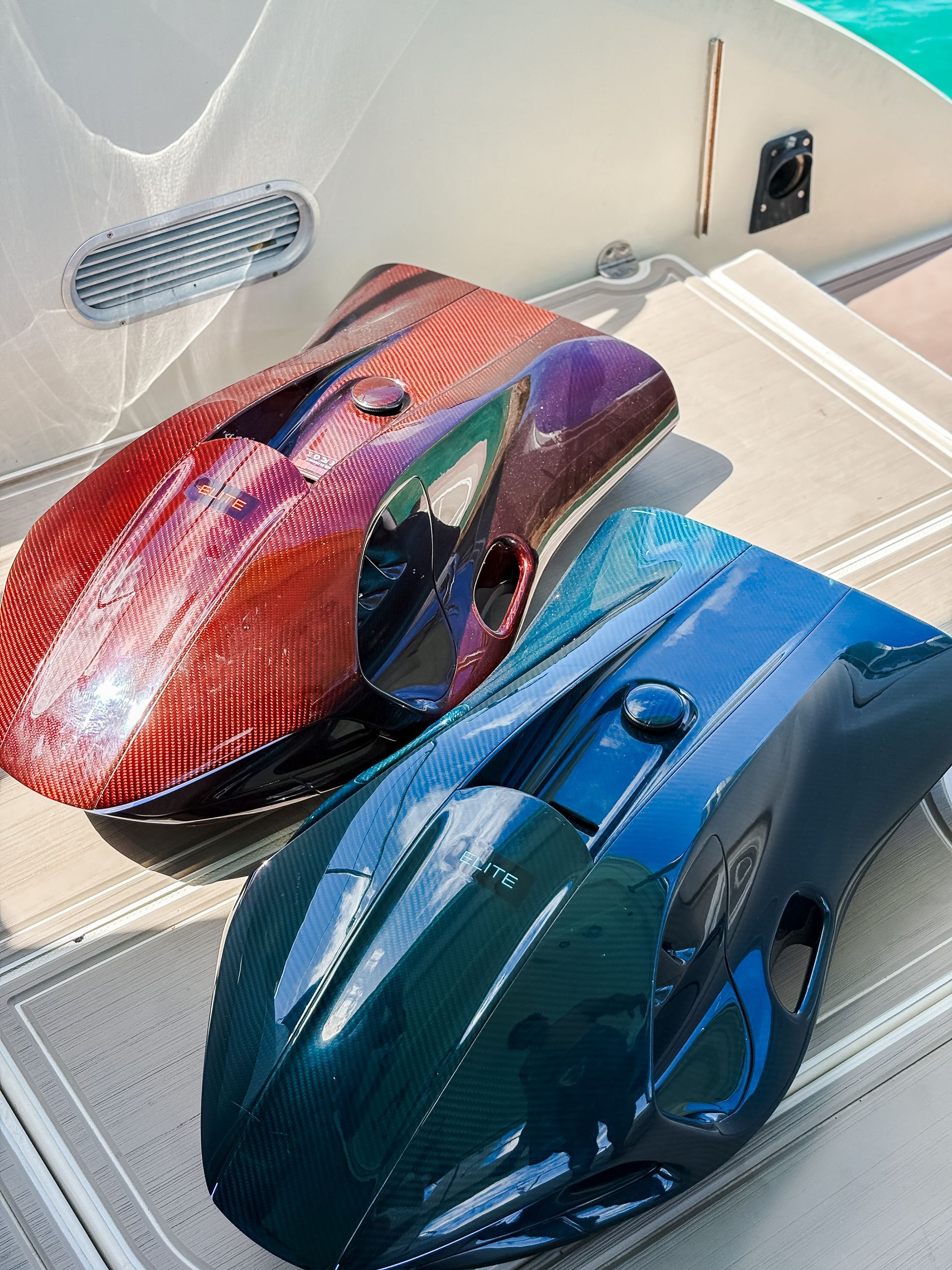 Two underwater scooters, red and blue, on a boat deck.