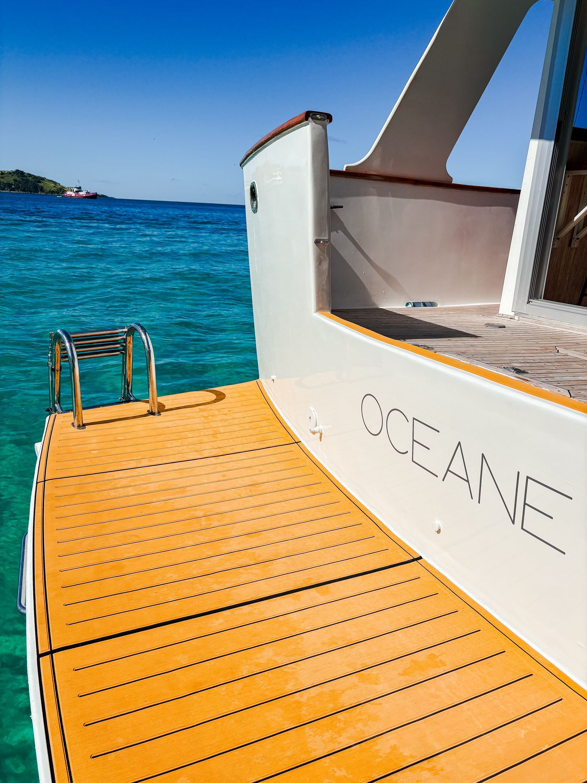 A white boat with wooden deck, steps, and ladder in clear blue water; 