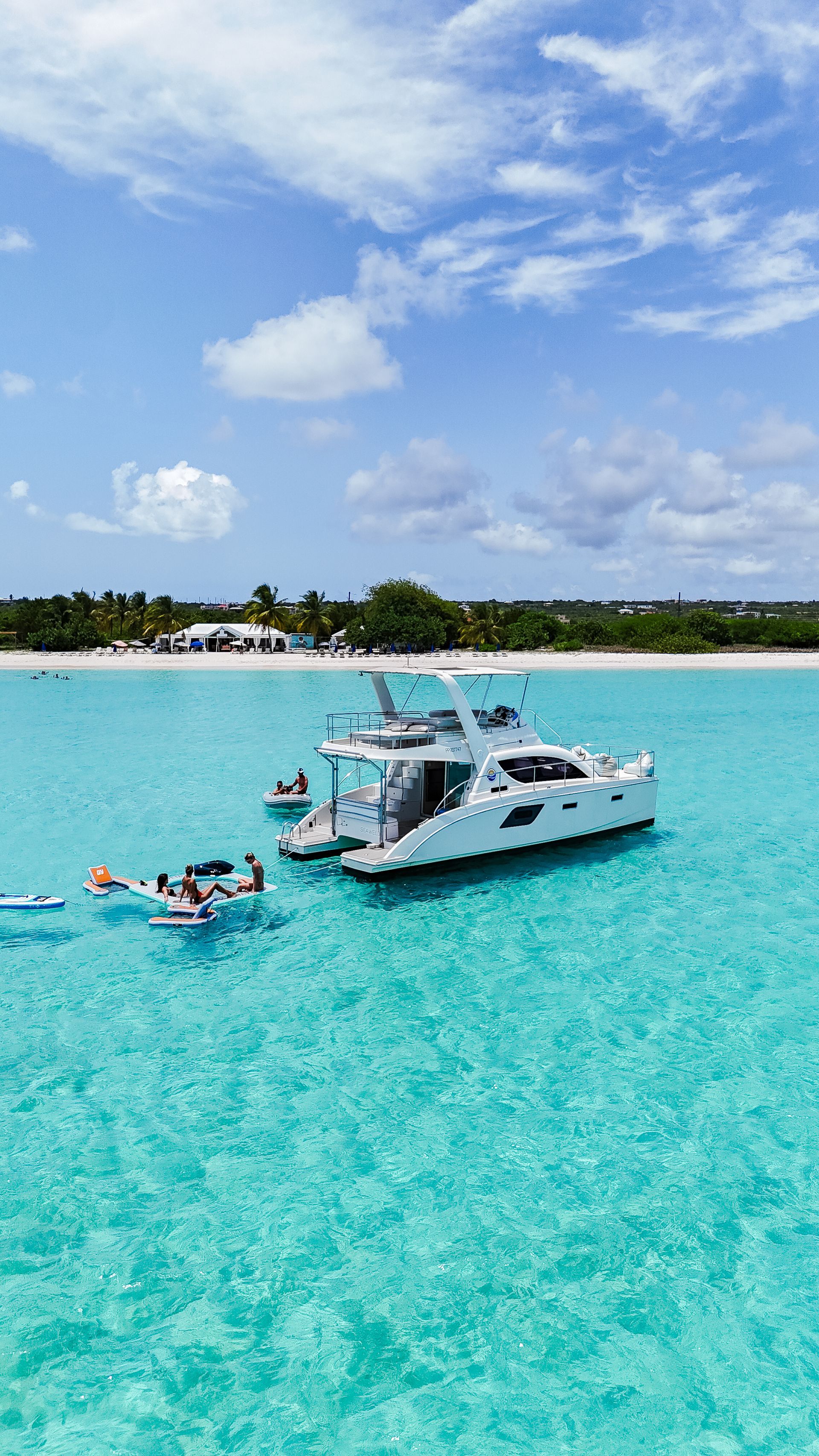 White catamaran in turquoise water near a beach under a blue sky.