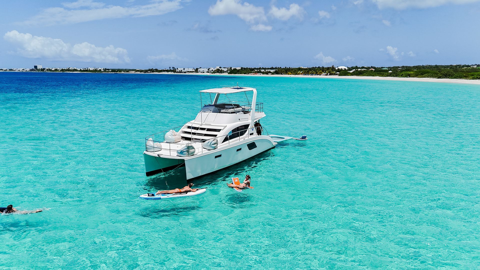 White catamaran in turquoise water; people swimming and on a paddleboard.