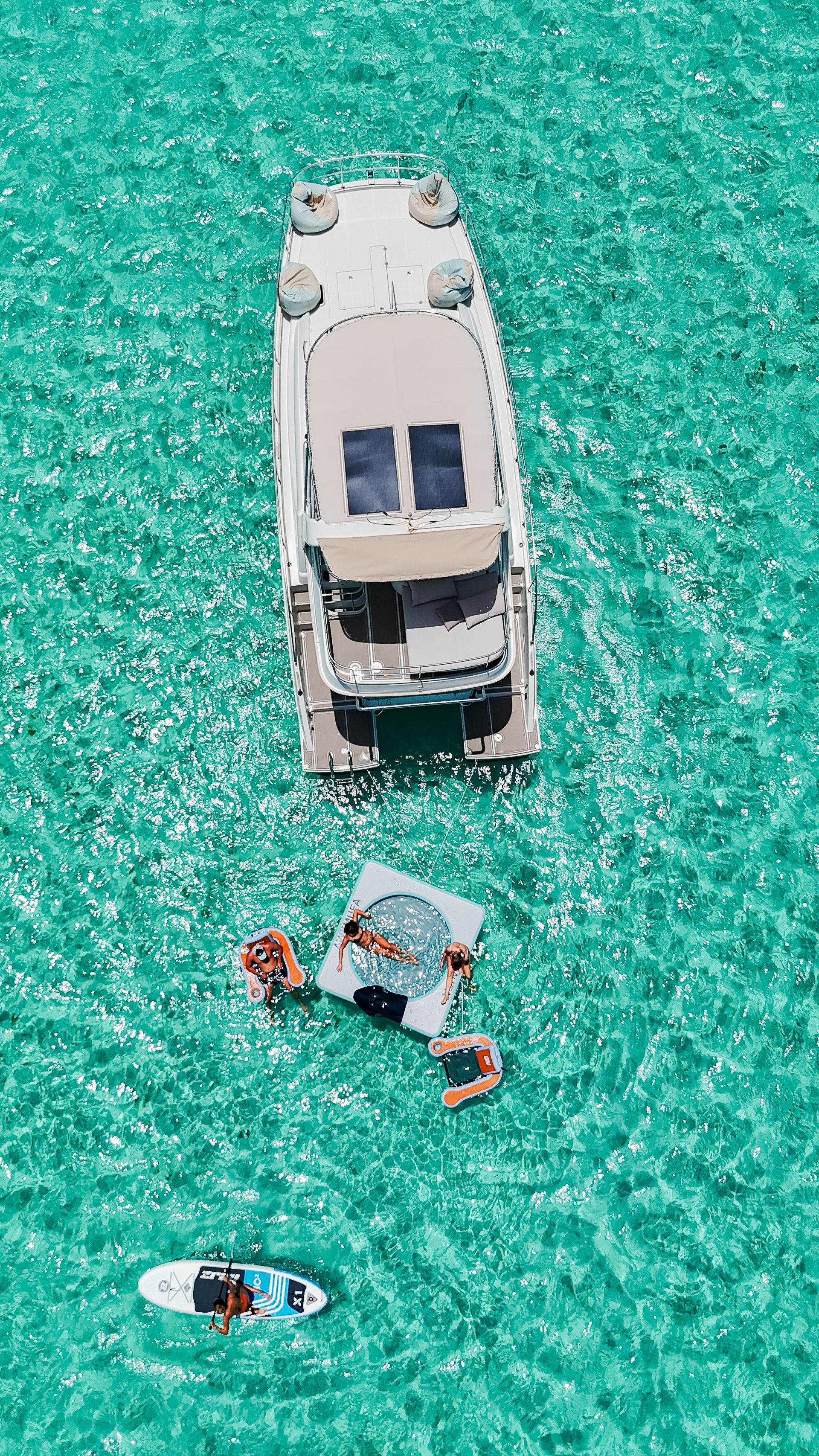 Yacht and raft in turquoise water. People relax on the raft and paddleboard.