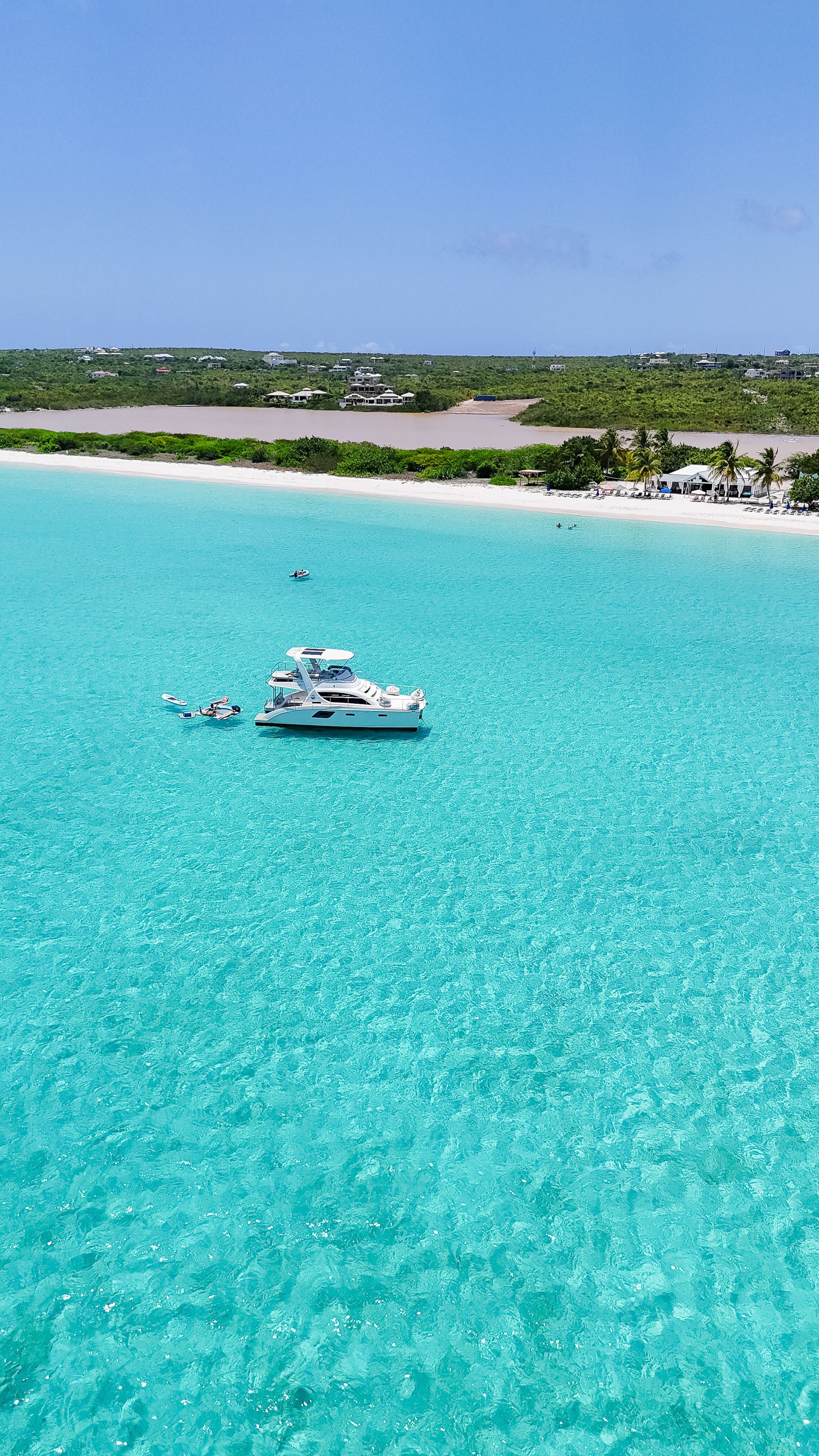 Boat in turquoise water near a sandy beach with lush green vegetation.