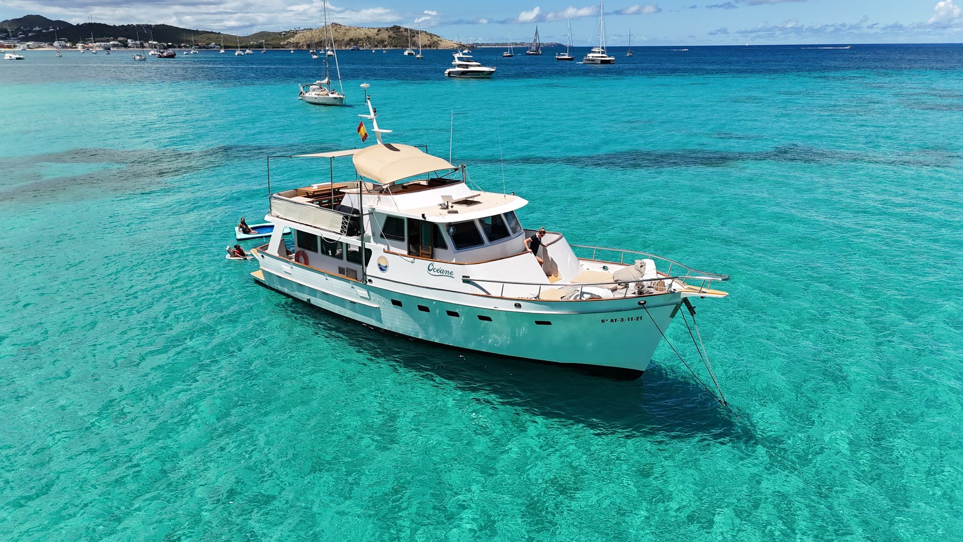 White yacht floating in turquoise water near a sandy beach under a blue sky.