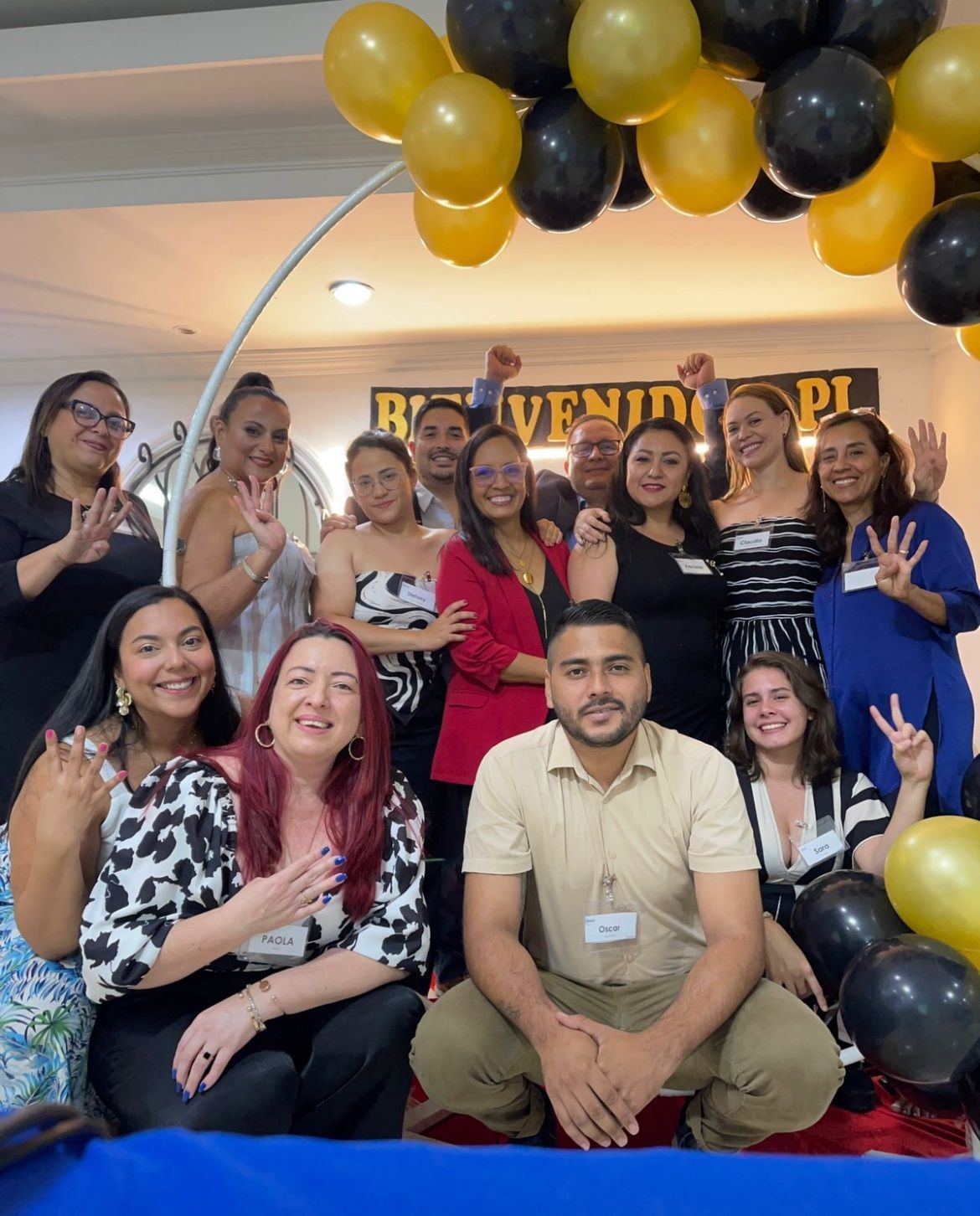 Un grupo de personas posa para una foto bajo un arco de globos negros y dorados durante un evento