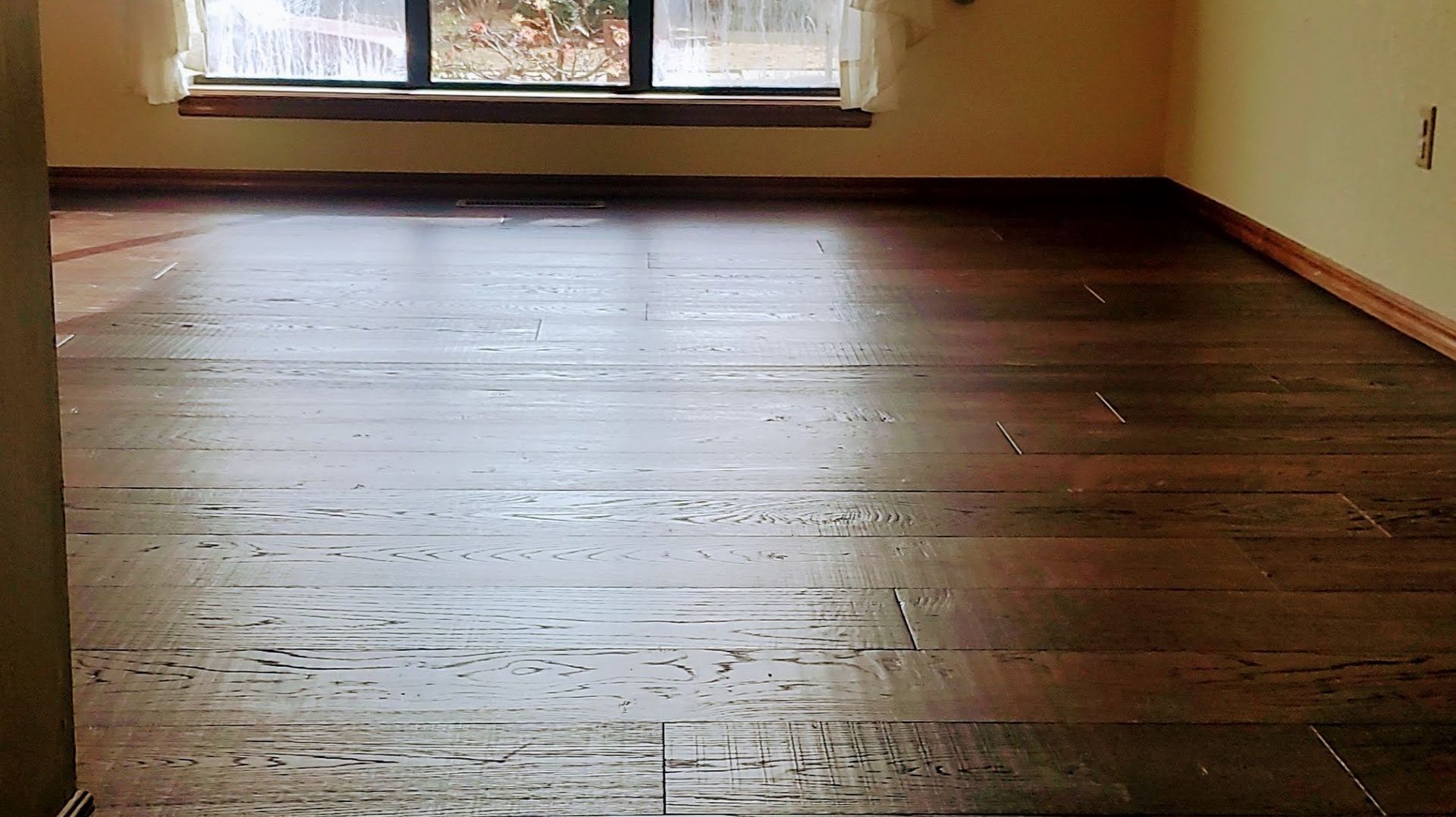 Empty room with dark hardwood floors and a large window at the far wall.