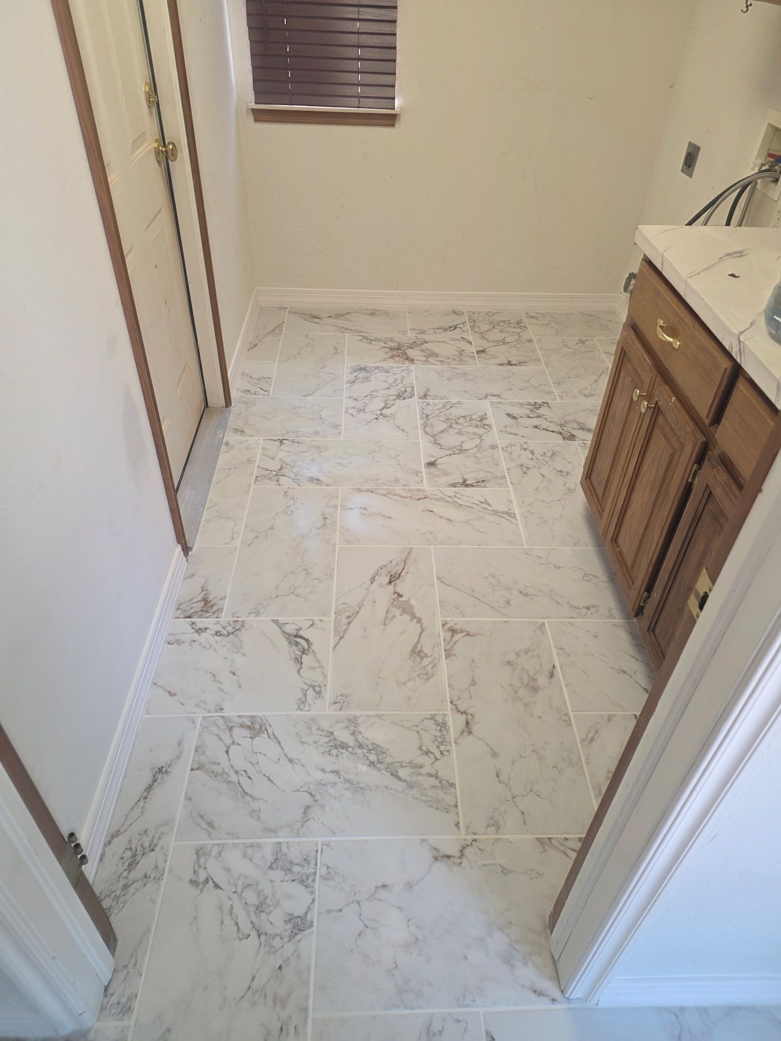Small bathroom with marble tile floor, vanity on the right, and window with blinds at the far wall