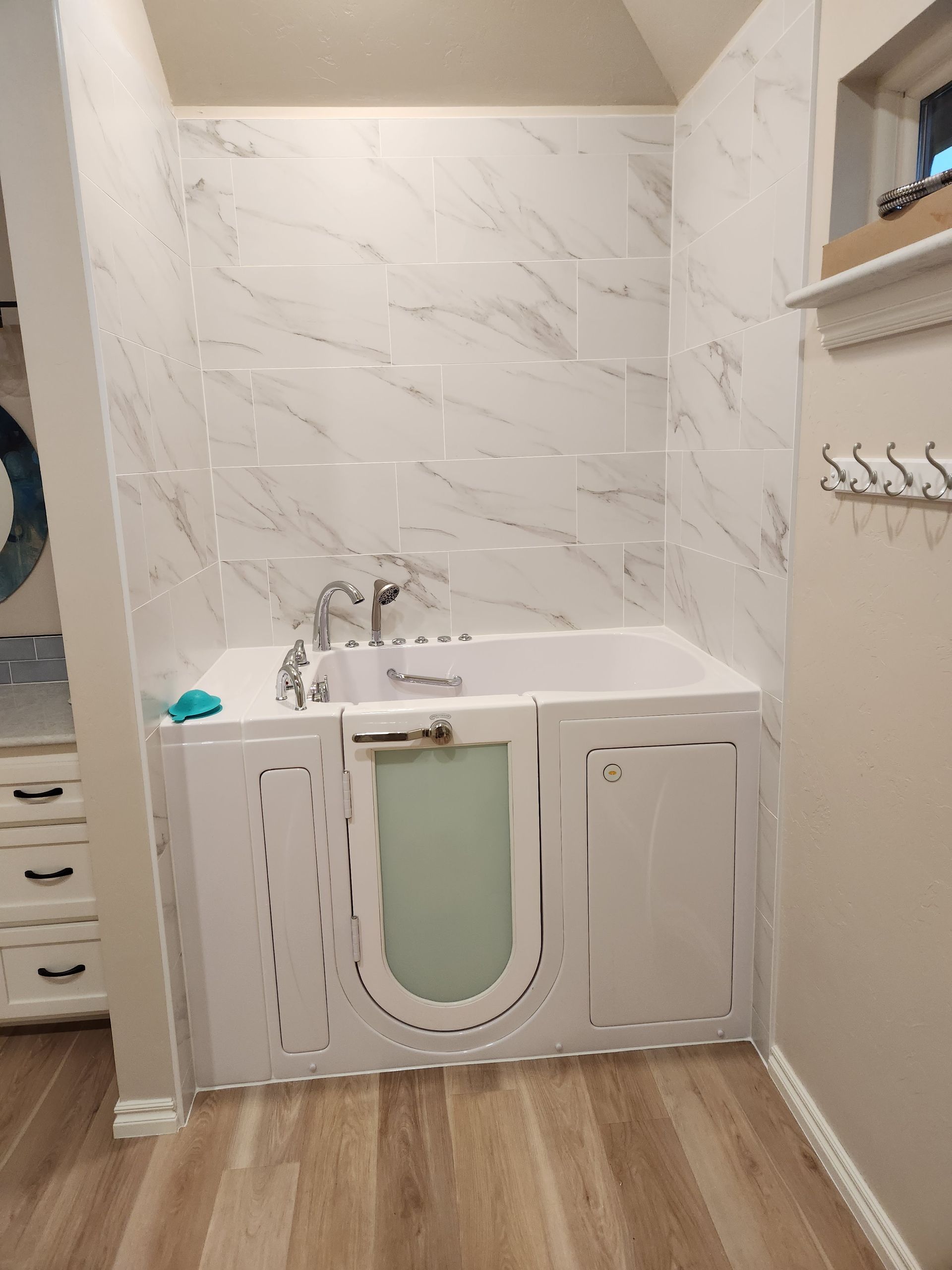 Small bathroom vanity with white cabinet, marble-look wall, and wood floor.