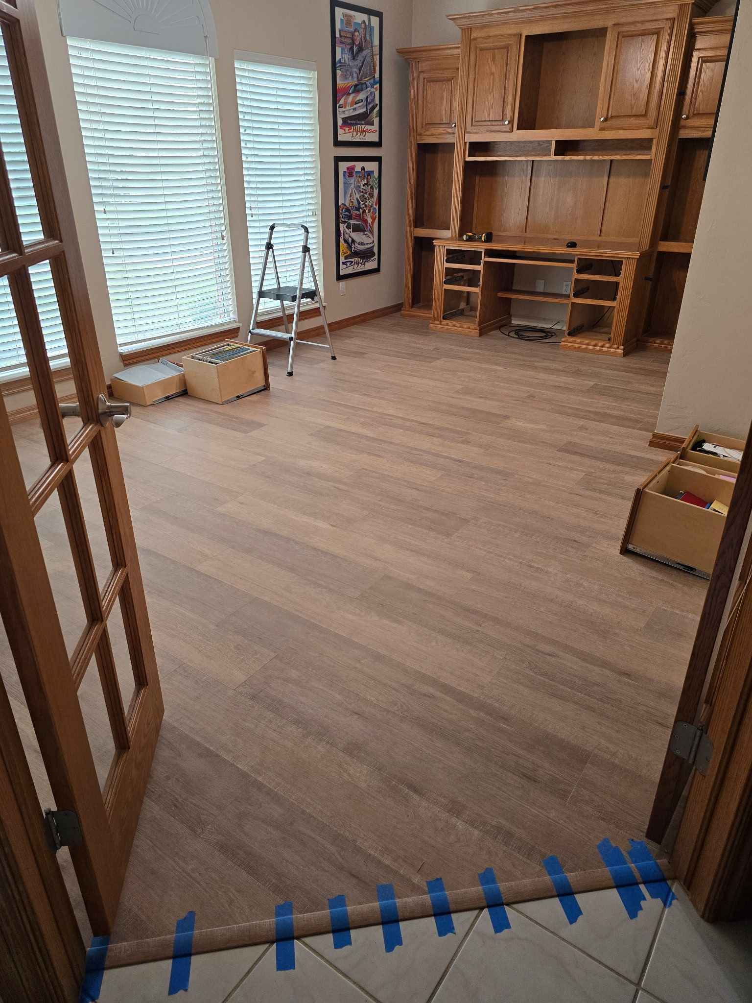 Empty room with wood floor, large windows, and built-in wooden shelves along the back wall.