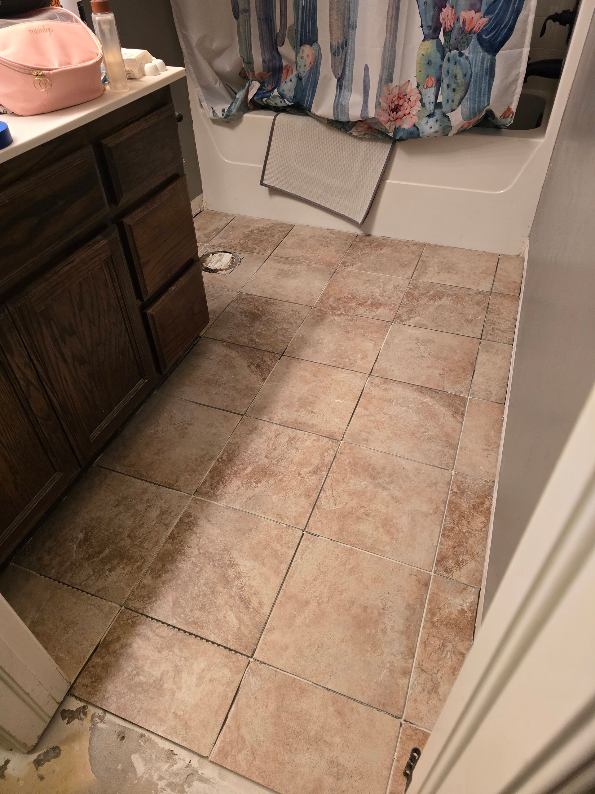 Bathroom with tan tile floor, dark vanity, and floral shower curtain hanging in the corner.