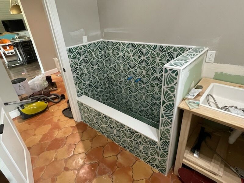 Small bathroom under renovation with green patterned tile wainscoting and exposed sink cabinet.