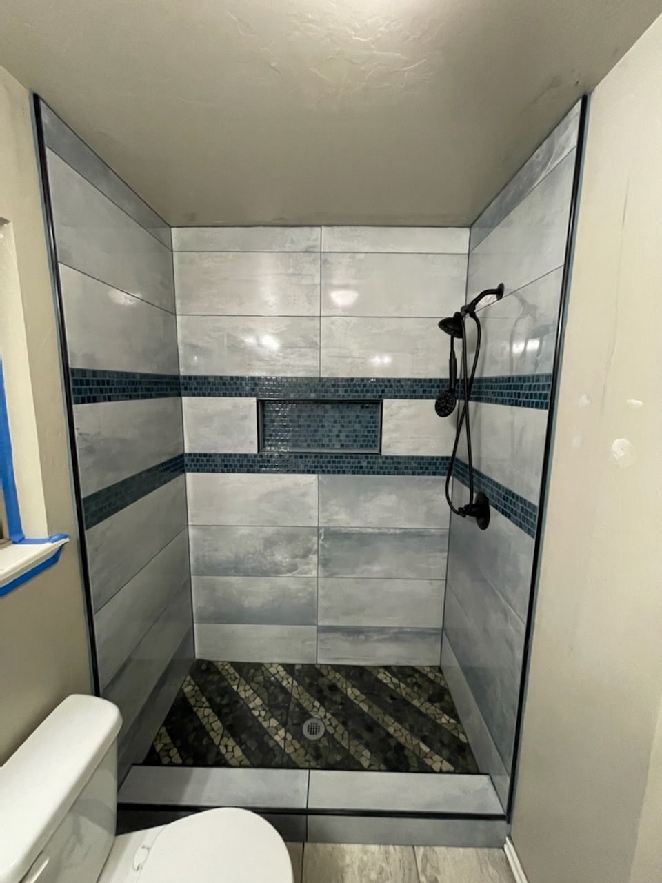 Walk-in shower with gray tile walls, dark striped floor, and handheld showerhead