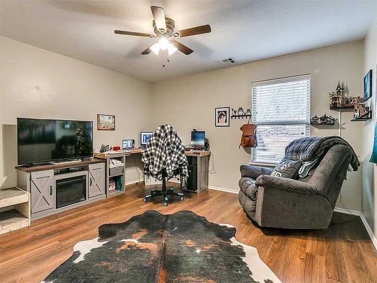 Living room office with TV, desk, recliner, and black-and-white rug under a ceiling fan.