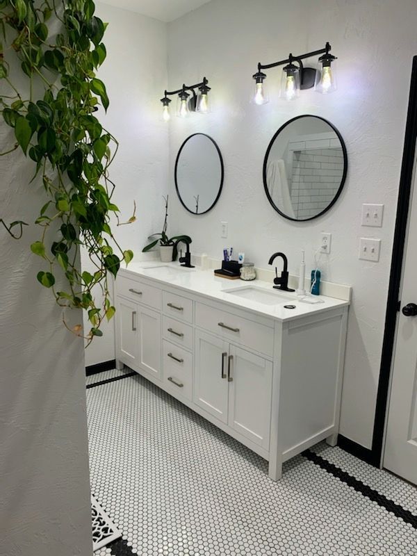 Modern white bathroom vanity with double round mirrors, black fixtures, and hanging greenery