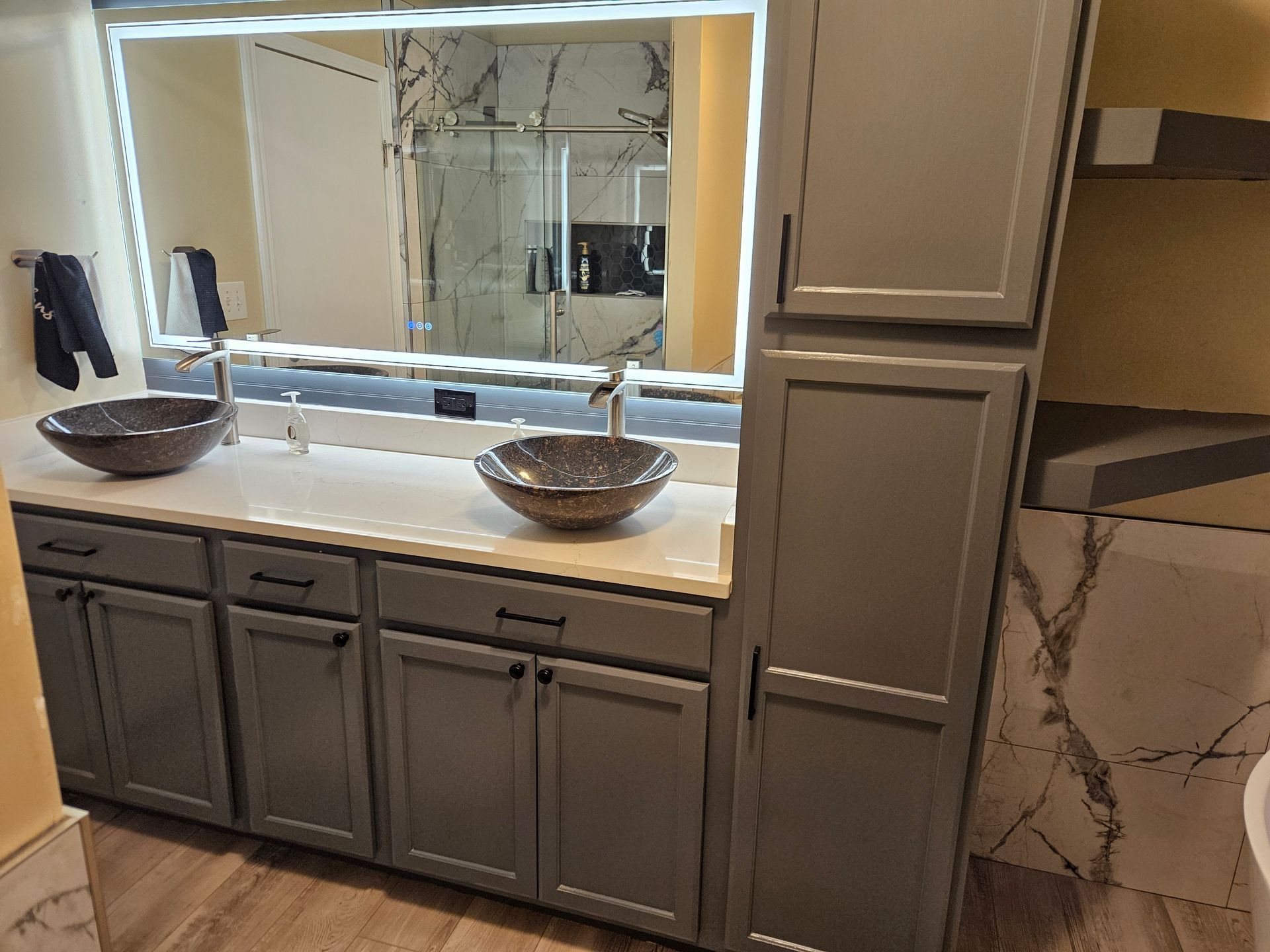 Modern bathroom vanity with double vessel sinks, large mirror, and gray cabinets under warm lighting