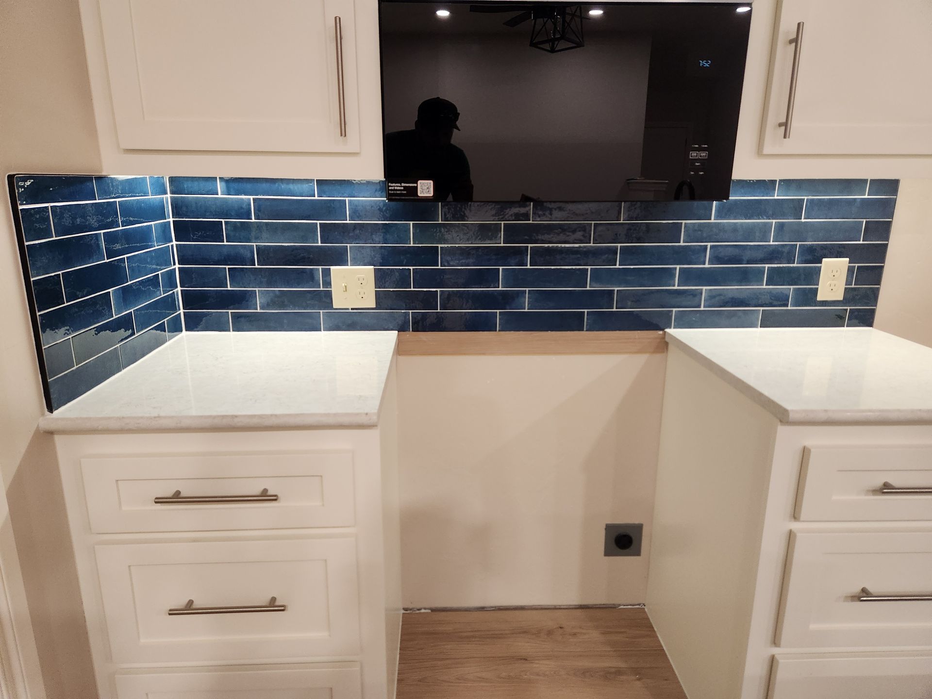 White kitchen desk nook with blue tile backsplash, cabinets, countertop, and wall-mounted TV above.