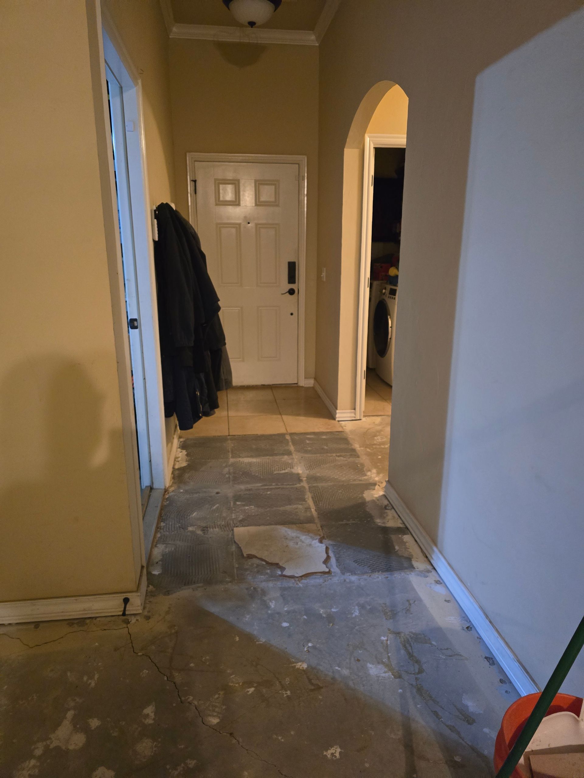 Hallway with damaged flooring and exposed underlayment near a white door and archway.