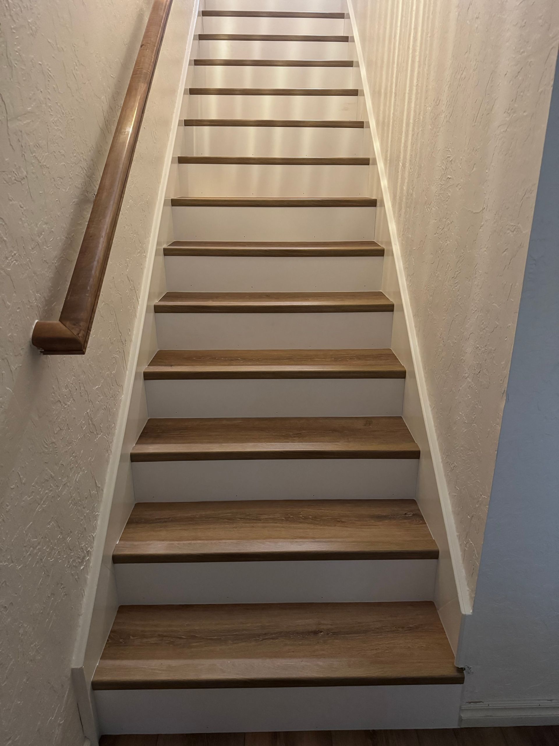 Narrow indoor staircase with wooden steps, white walls, and a handrail on the left.