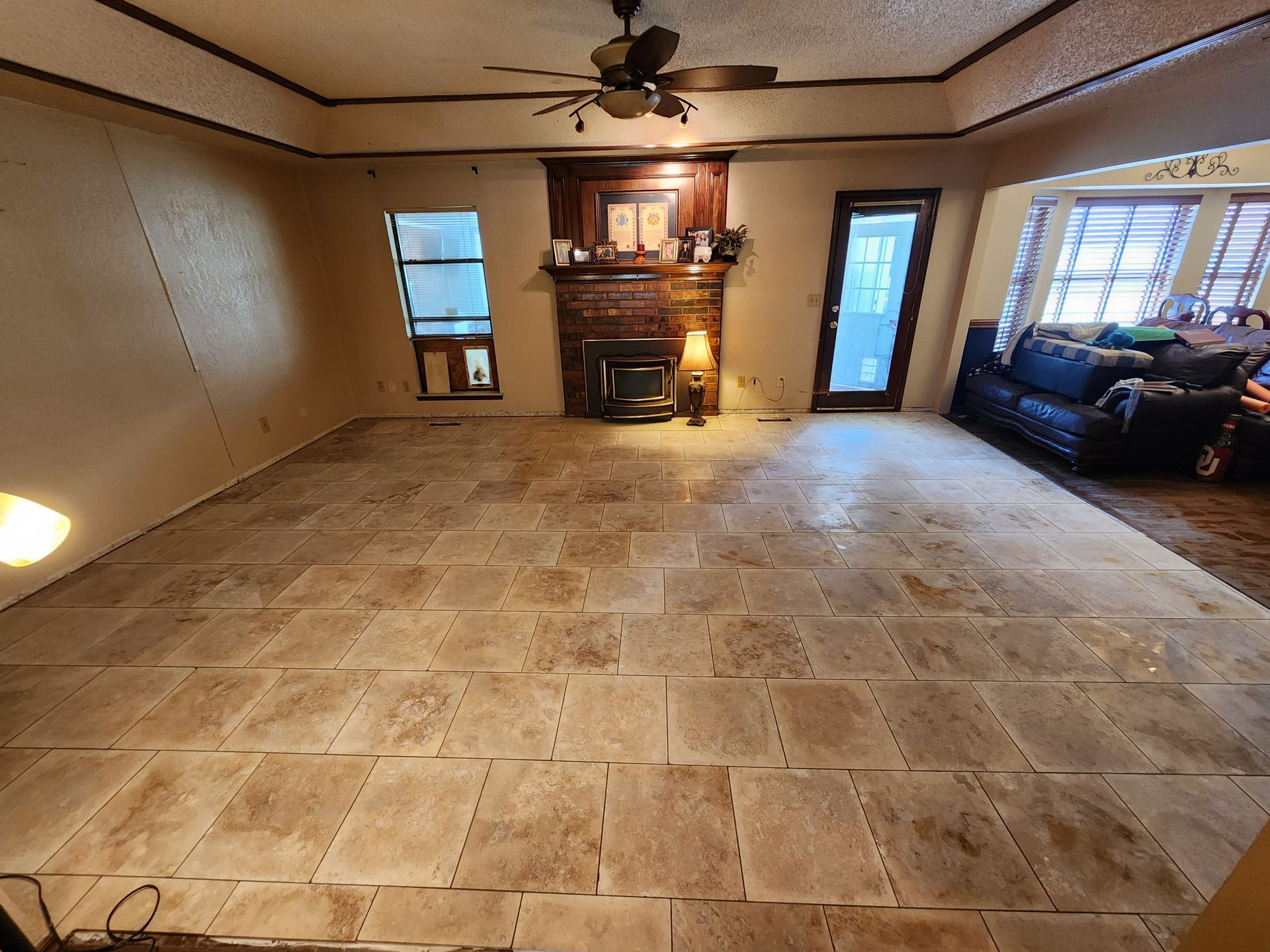 Spacious living room with tan tile floor, fireplace, ceiling fan, and a couch by the window.