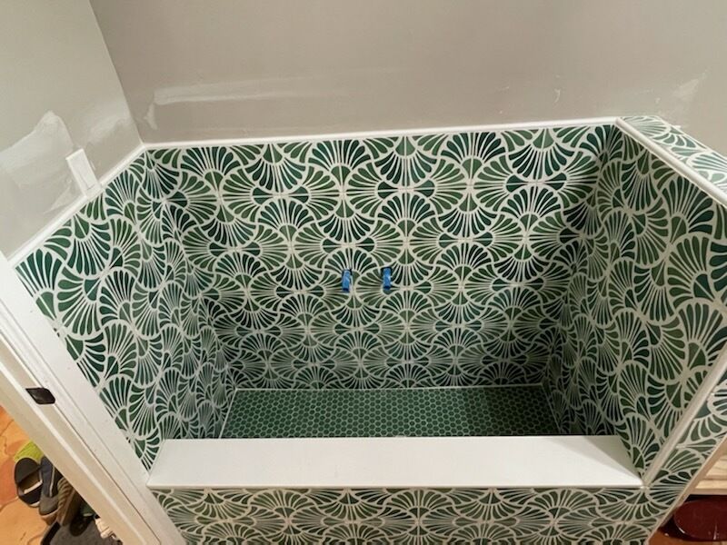 Green patterned tile bathtub alcove with a white tub and blue shower fixtures