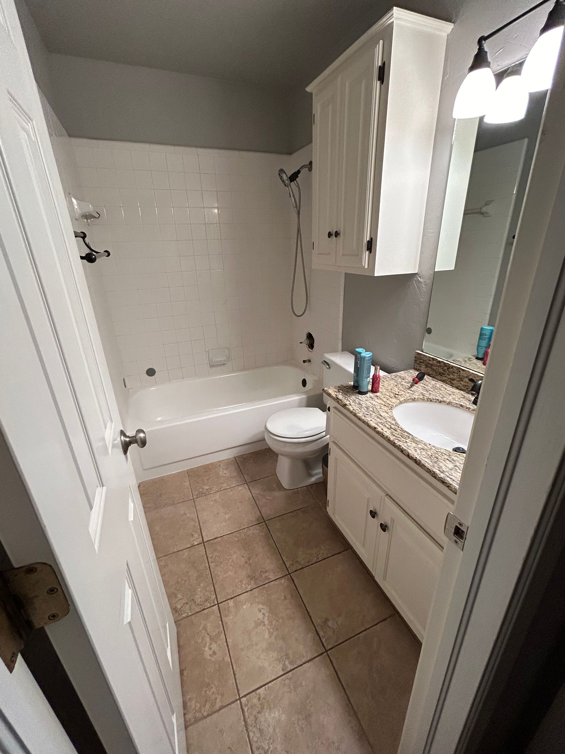 Small beige bathroom with tub, toilet, vanity, and mirrored cabinets.
