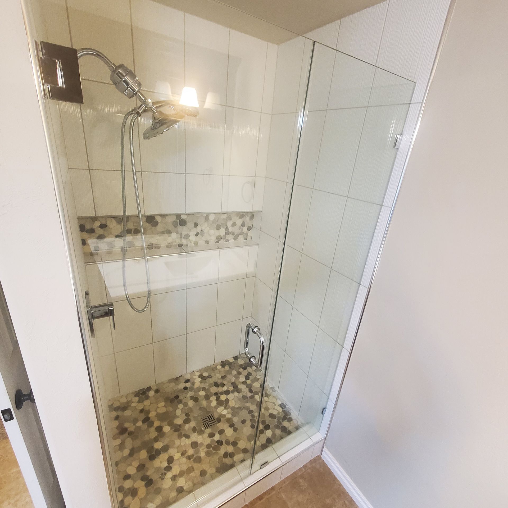 Tiled glass shower with mosaic floor, built-in shelf, and chrome showerhead in a bathroom