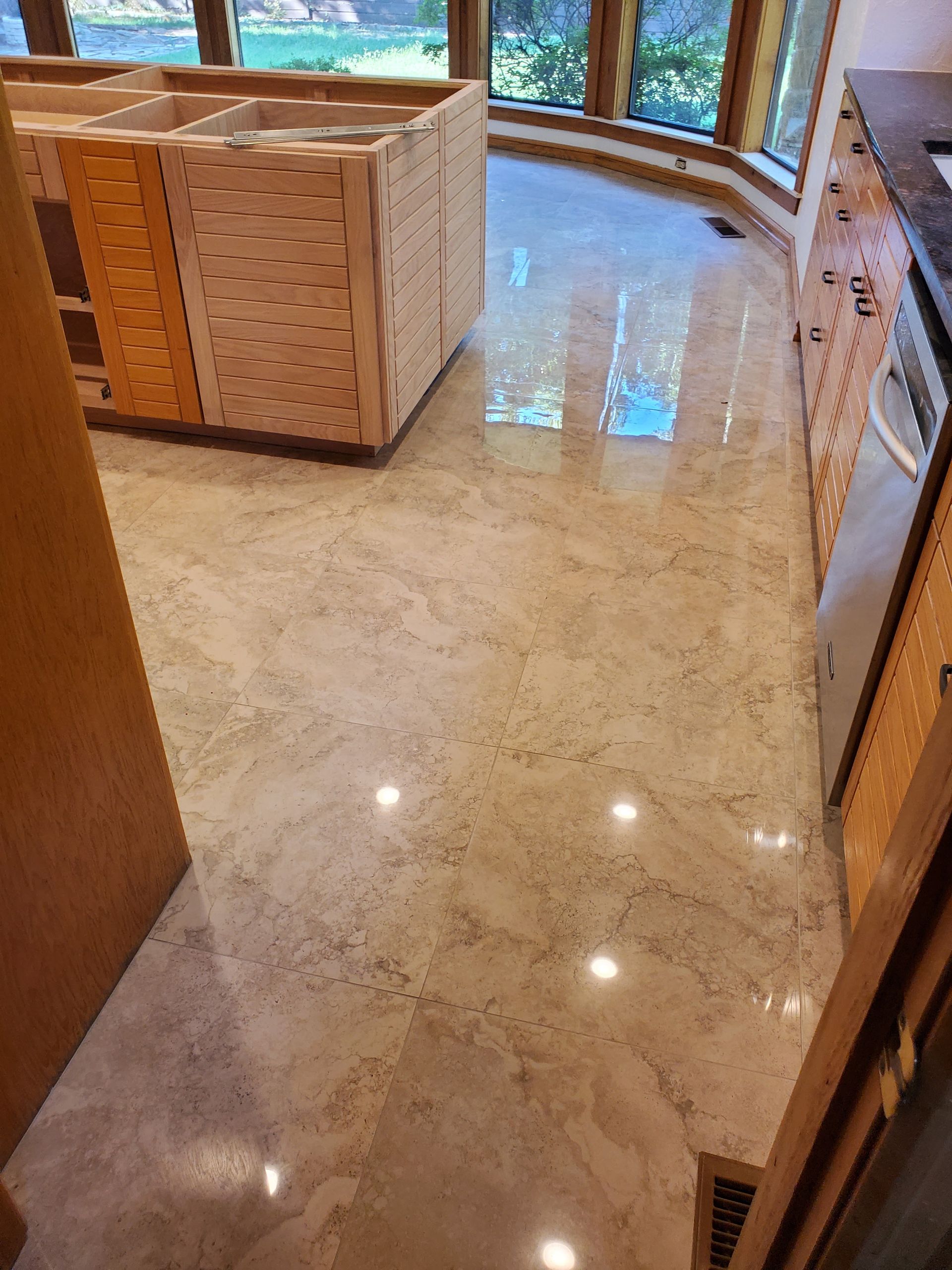 Polished cream marble floor in a bright kitchen or hallway with wooden cabinets and windows.