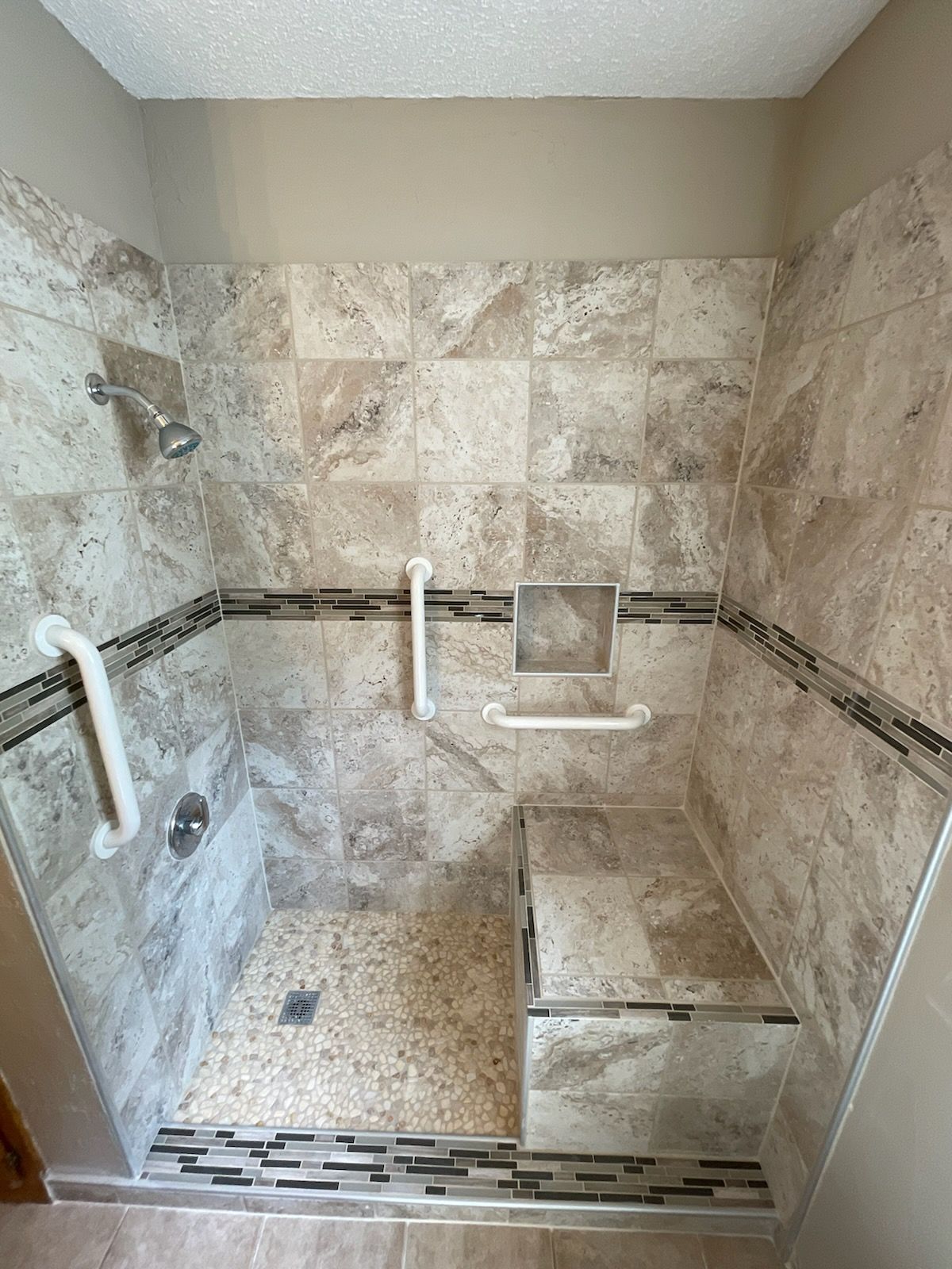 Walk-in shower with beige tile, grab bars, and built-in bench seat