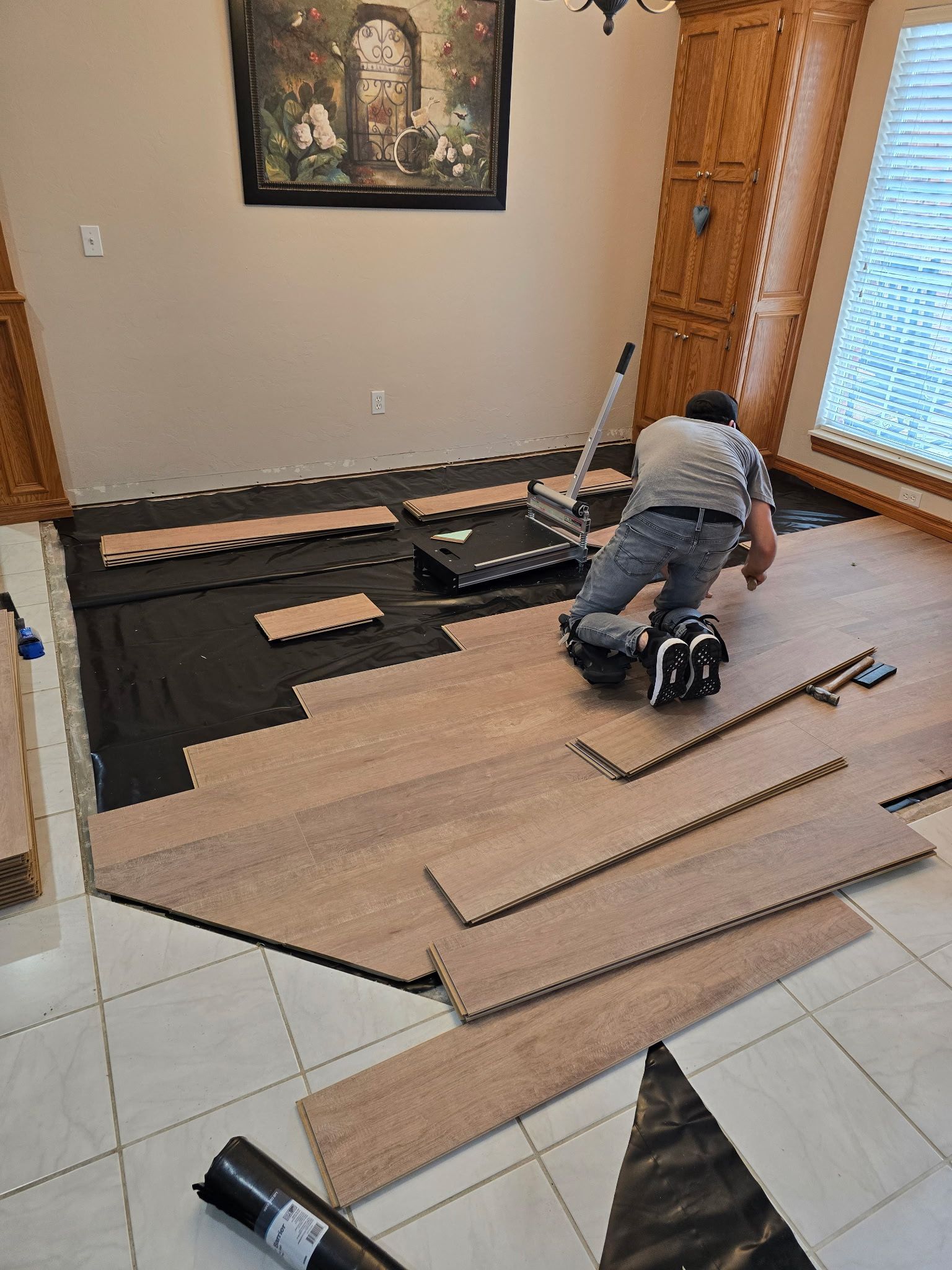 Person kneeling on floor installing black underlayment in a living room near a sliding door