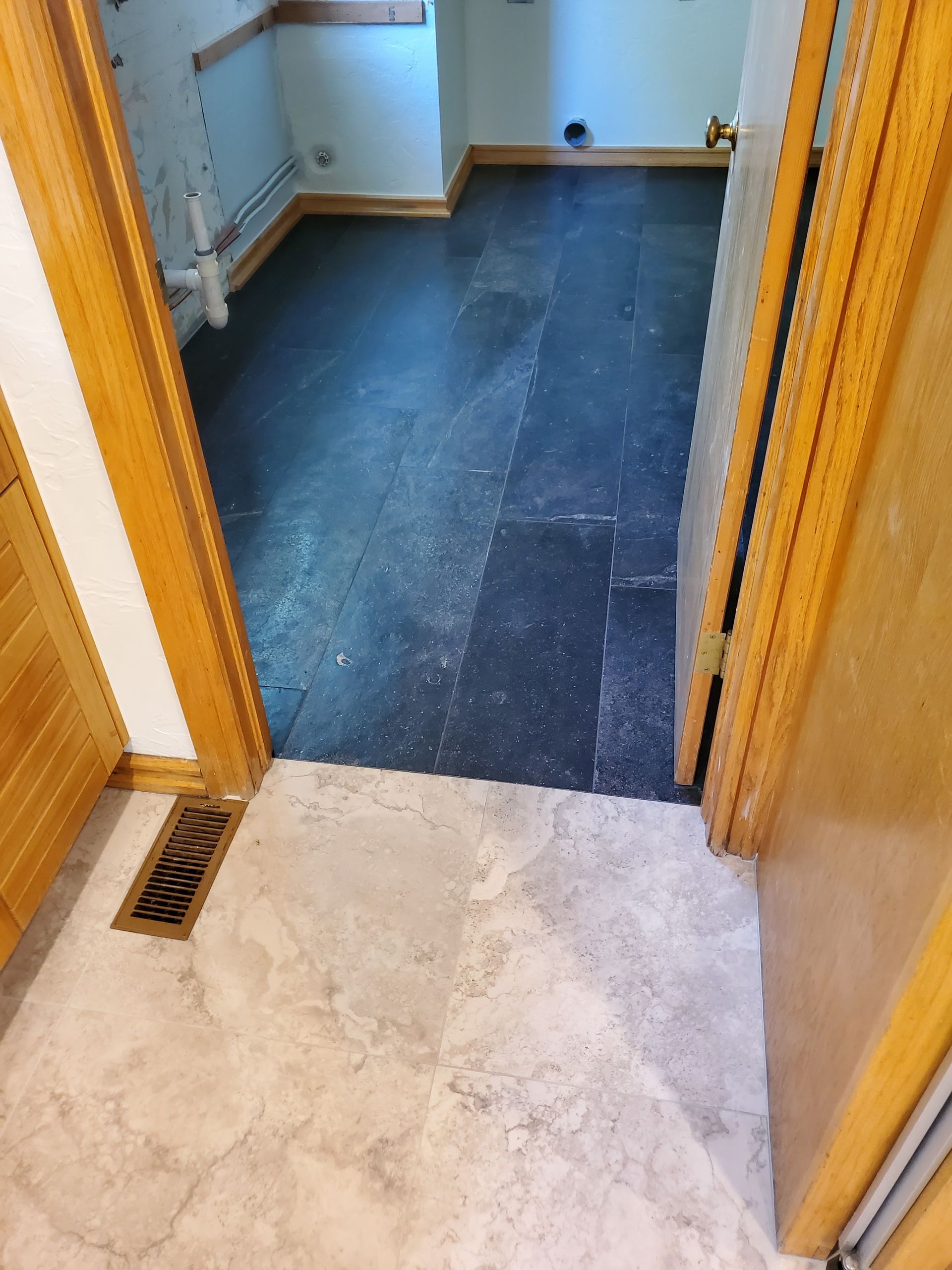 Threshold between beige tile and dark blue flooring in a narrow hallway, with a floor vent on the left.