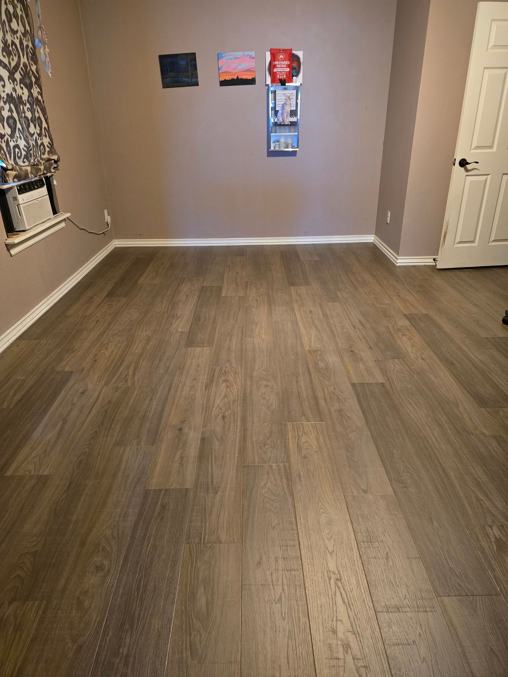 Empty room with wood-look flooring, beige walls, and wall art near a closet door.