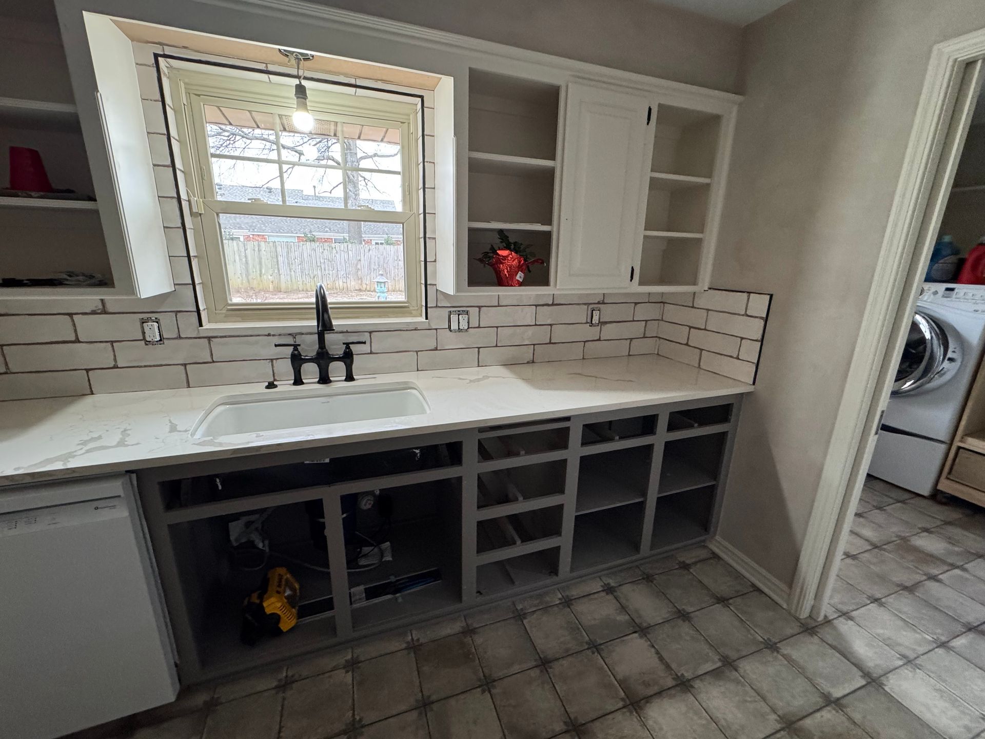 Kitchen sink area with white cabinets, subway tile backsplash, open shelves, and tiled floor under a window