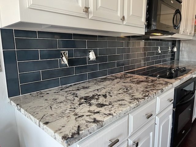 Modern kitchen countertop with blue subway tile backsplash and white cabinets, featuring a black oven and microwave.