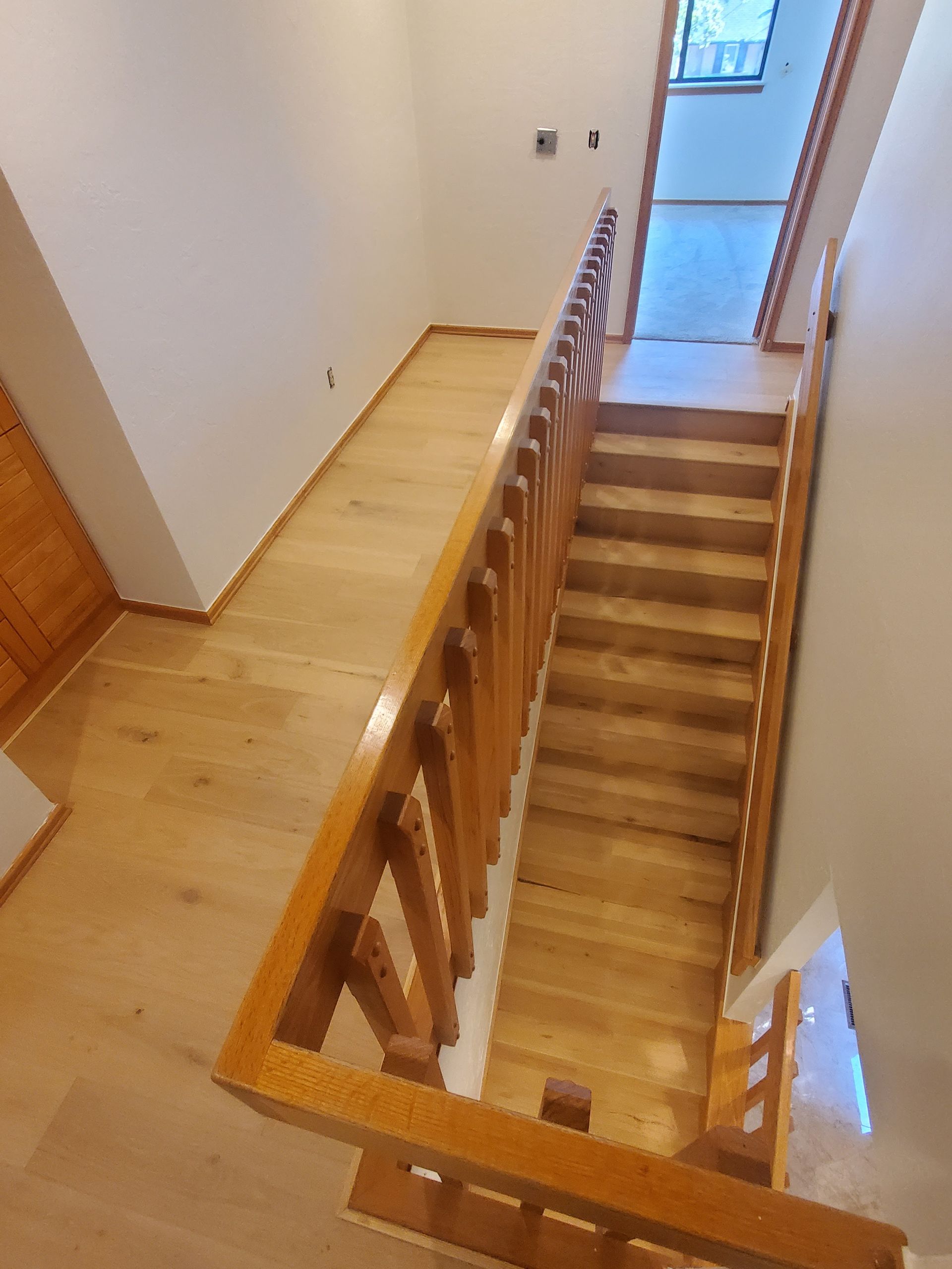 Wooden staircase with railing in a narrow indoor hallway, viewed from the top landing.