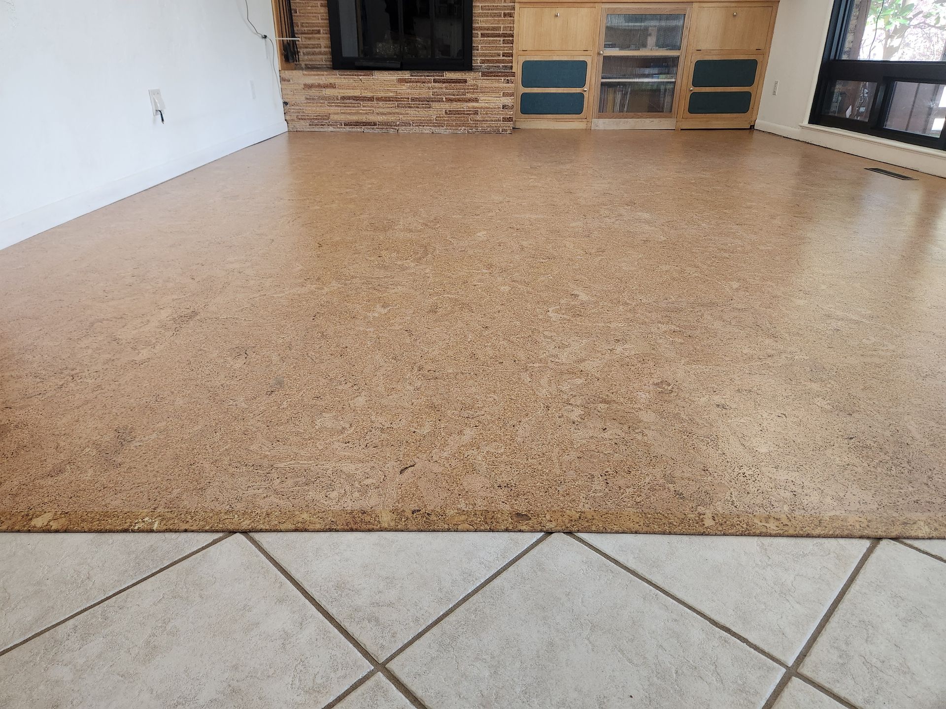 Empty tan-speckled floor in a room with a brick wall and tile foreground