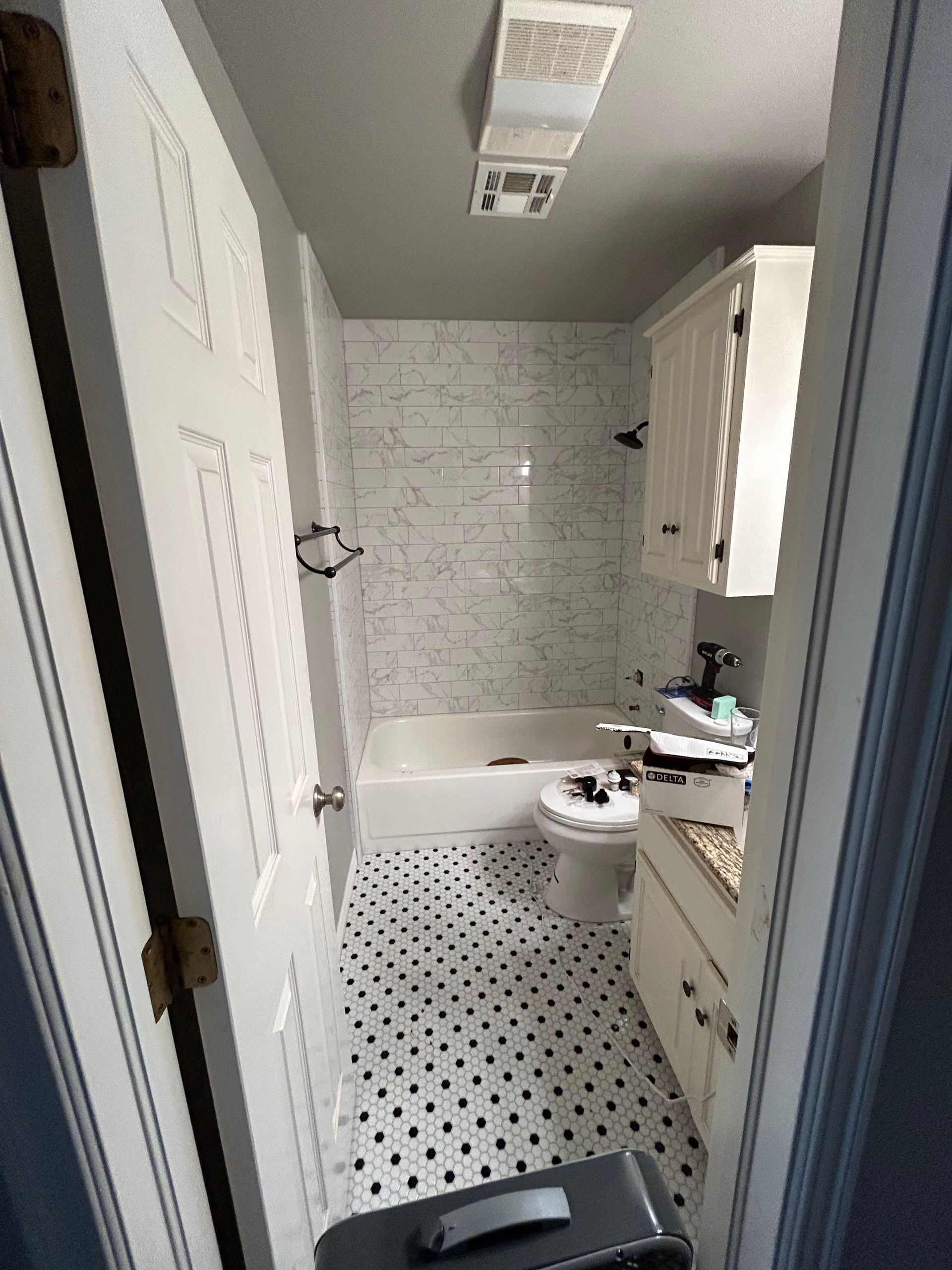 Small bathroom with white tile, bathtub, toilet, vanity, and black-and-white hexagon floor tiles.