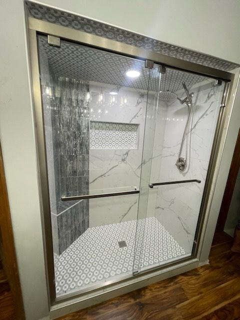 Modern glass shower enclosure with marble-look walls, hex tile floor, and chrome grab bar in a bathroom