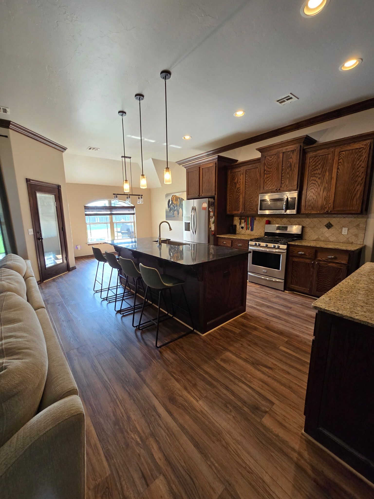 Open-concept kitchen with dark wood cabinets, black island, bar stools, and hardwood floors