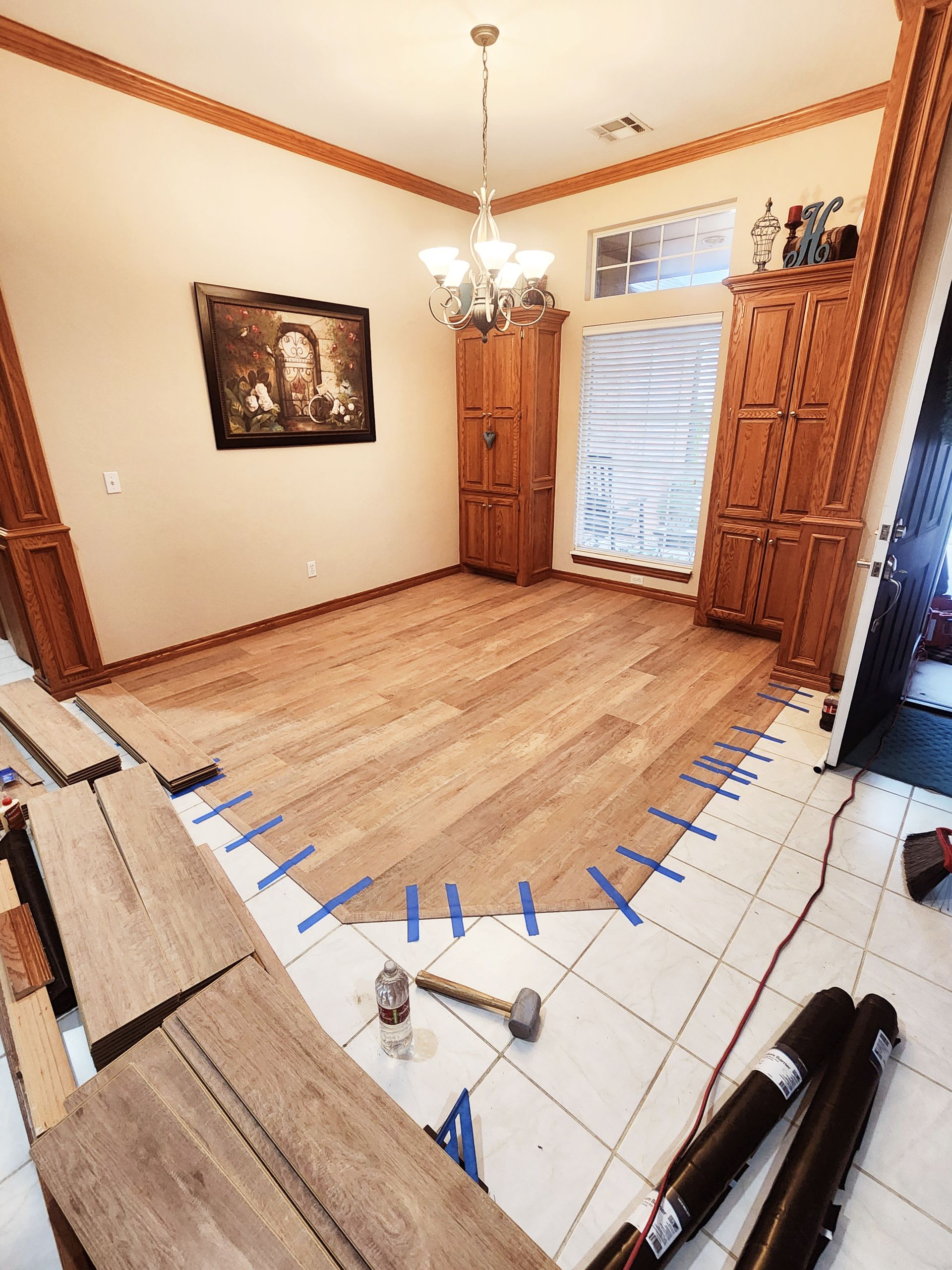 Dining room with hardwood floor, tiled border, chandelier, and wooden cabinets by a window